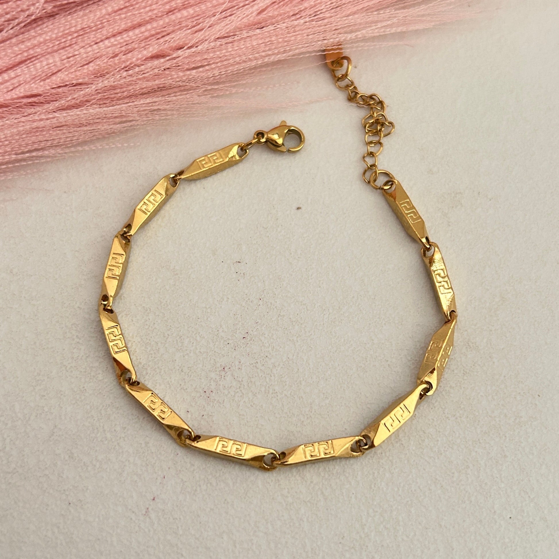Gold engraved bar link bracelet on pink background.