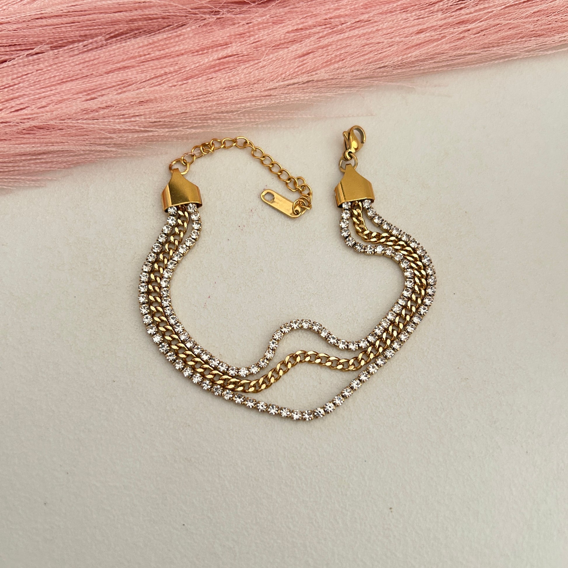 Layered gold and crystal chain bracelet displayed flat.