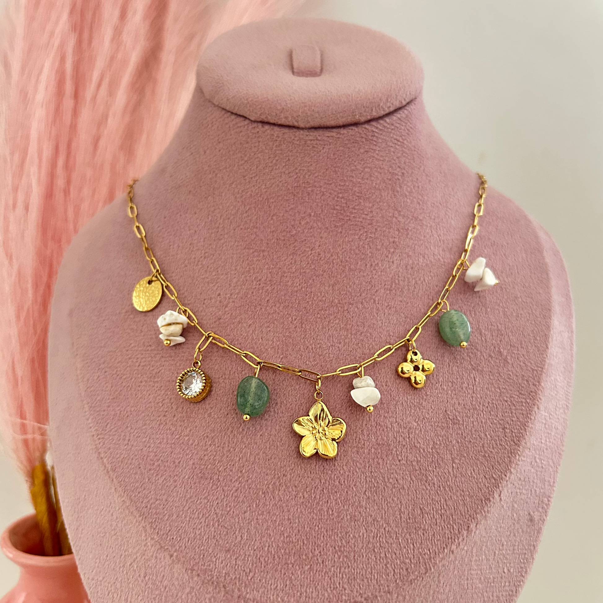 Gold charm necklace with green stones and flower pendant.