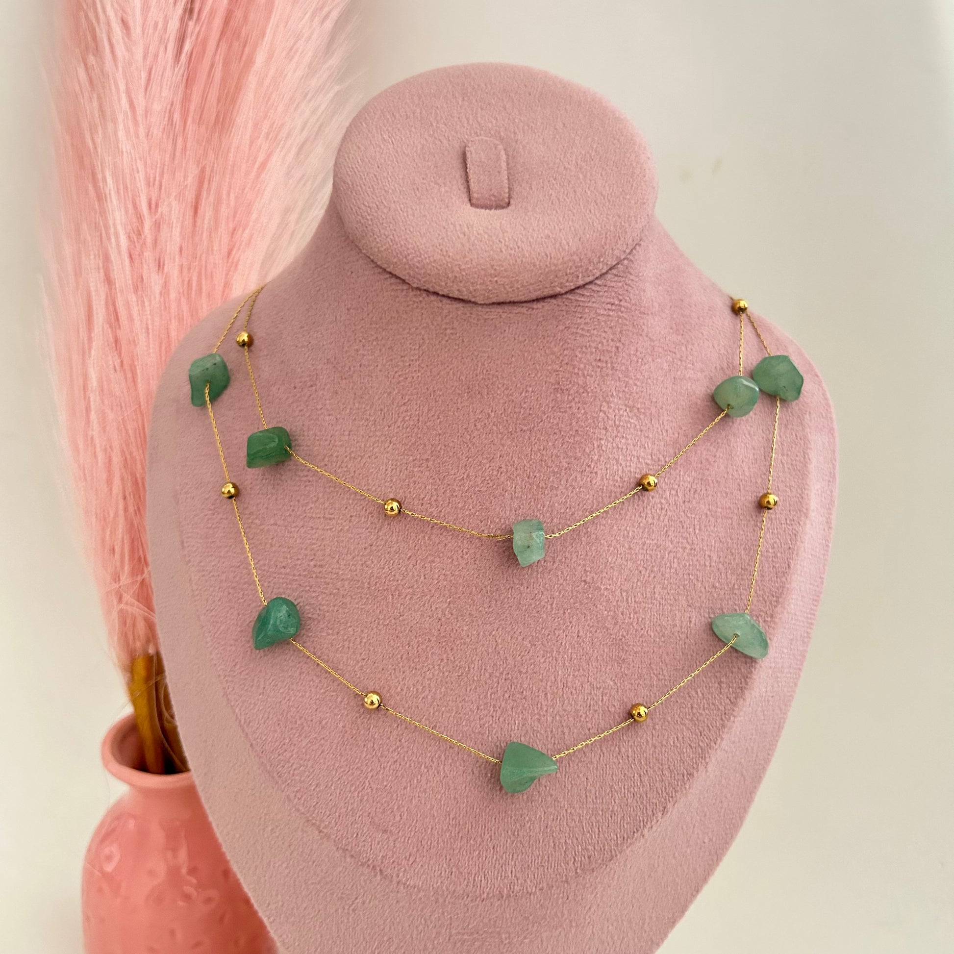 Double-layer gold necklace with green stone beads on pink background