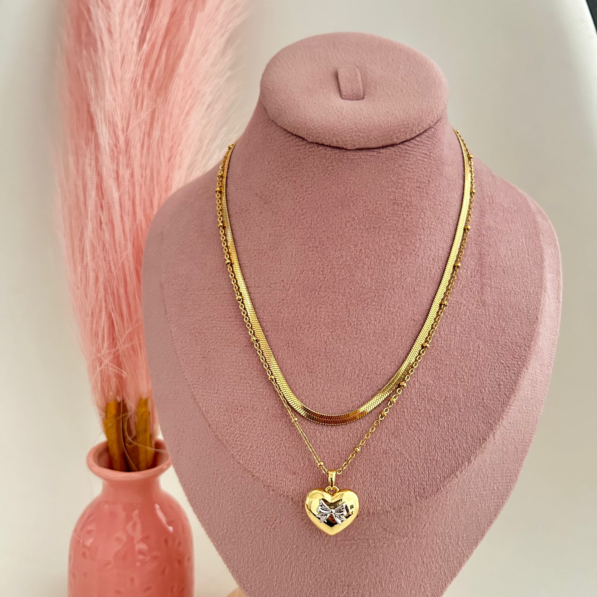 Double gold chain necklace with heart pendant on pink display