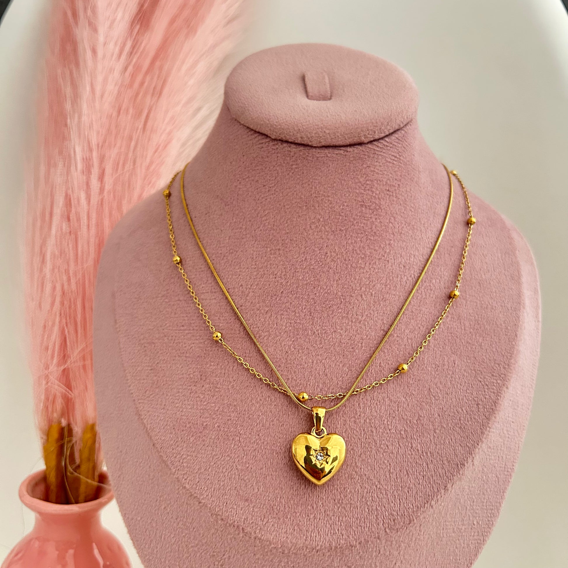 Double-layer gold necklace with shiny heart pendant on pink stand