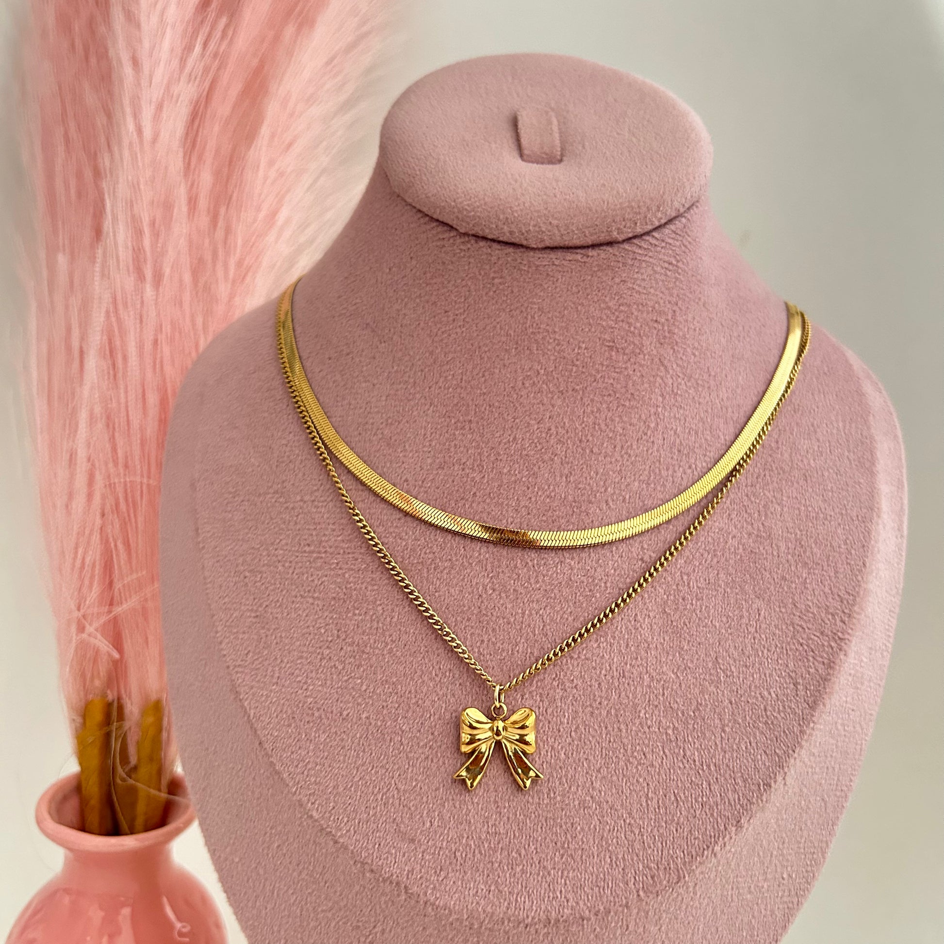 Layered gold necklace with bow pendant on pink stand
