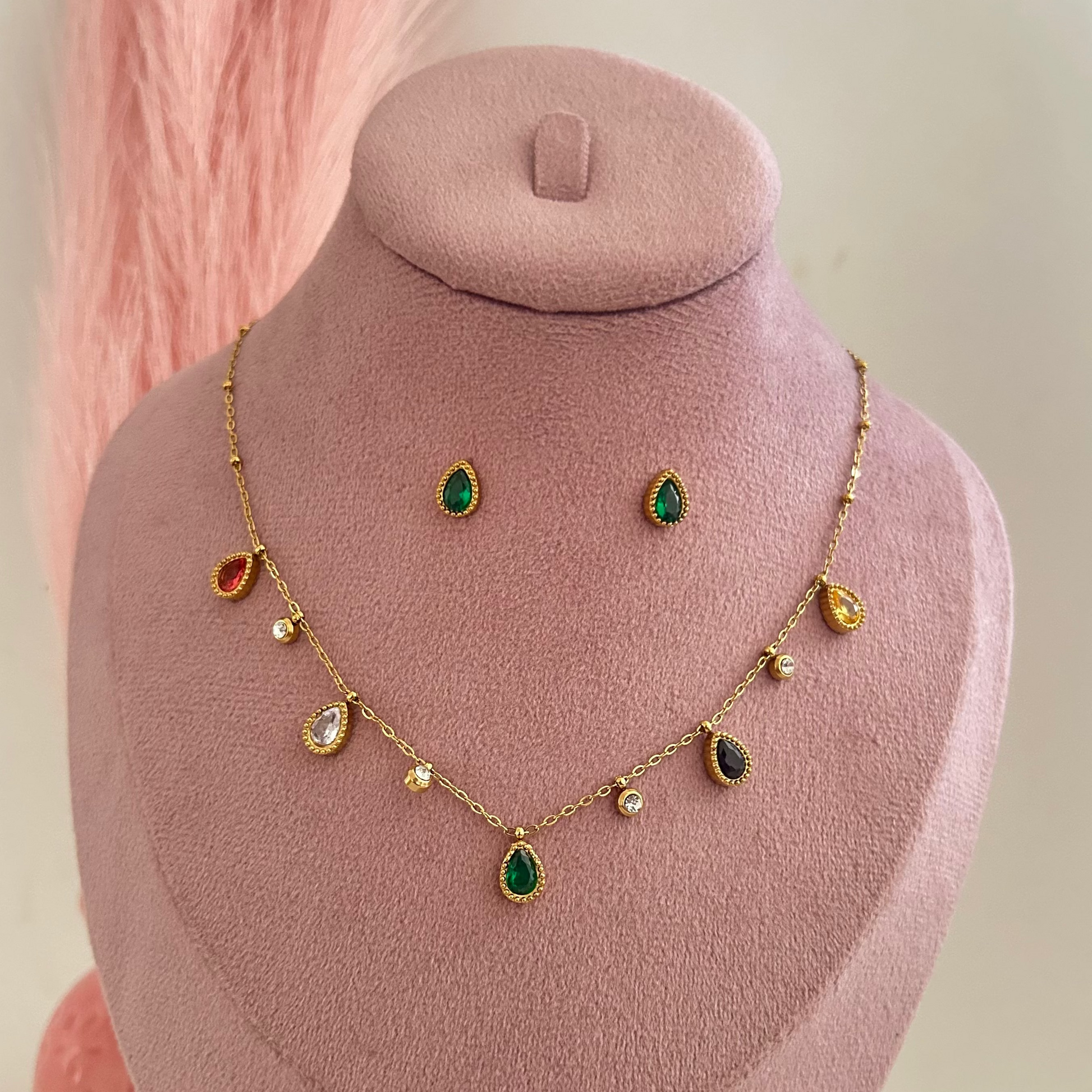 Gold necklace with multicolor teardrop charms and green pendant with matching earrings on pink display