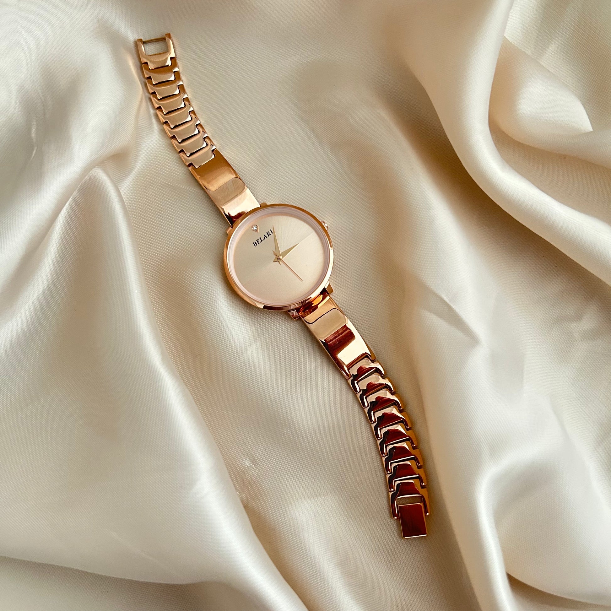 Rose gold wristwatch with round dial placed on satin fabric background.