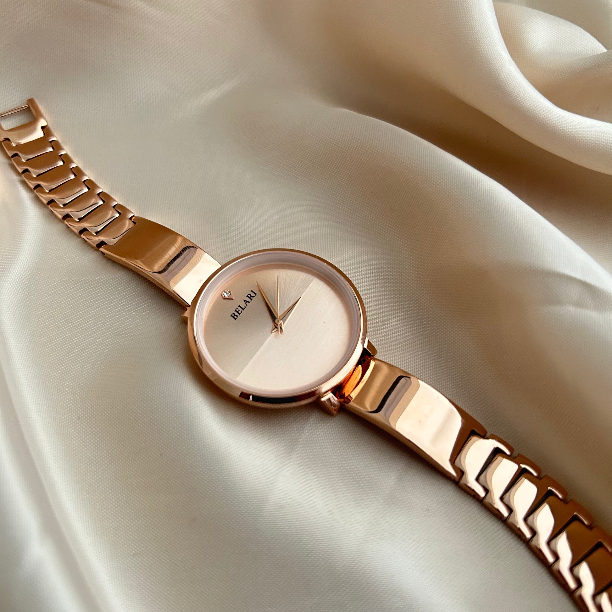 Rose gold wristwatch with round dial placed on satin fabric background.