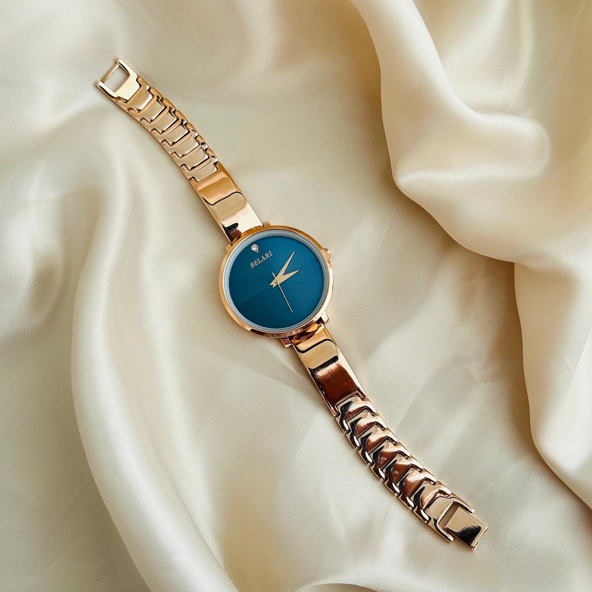 Rose gold wristwatch with round dial placed on satin fabric background.