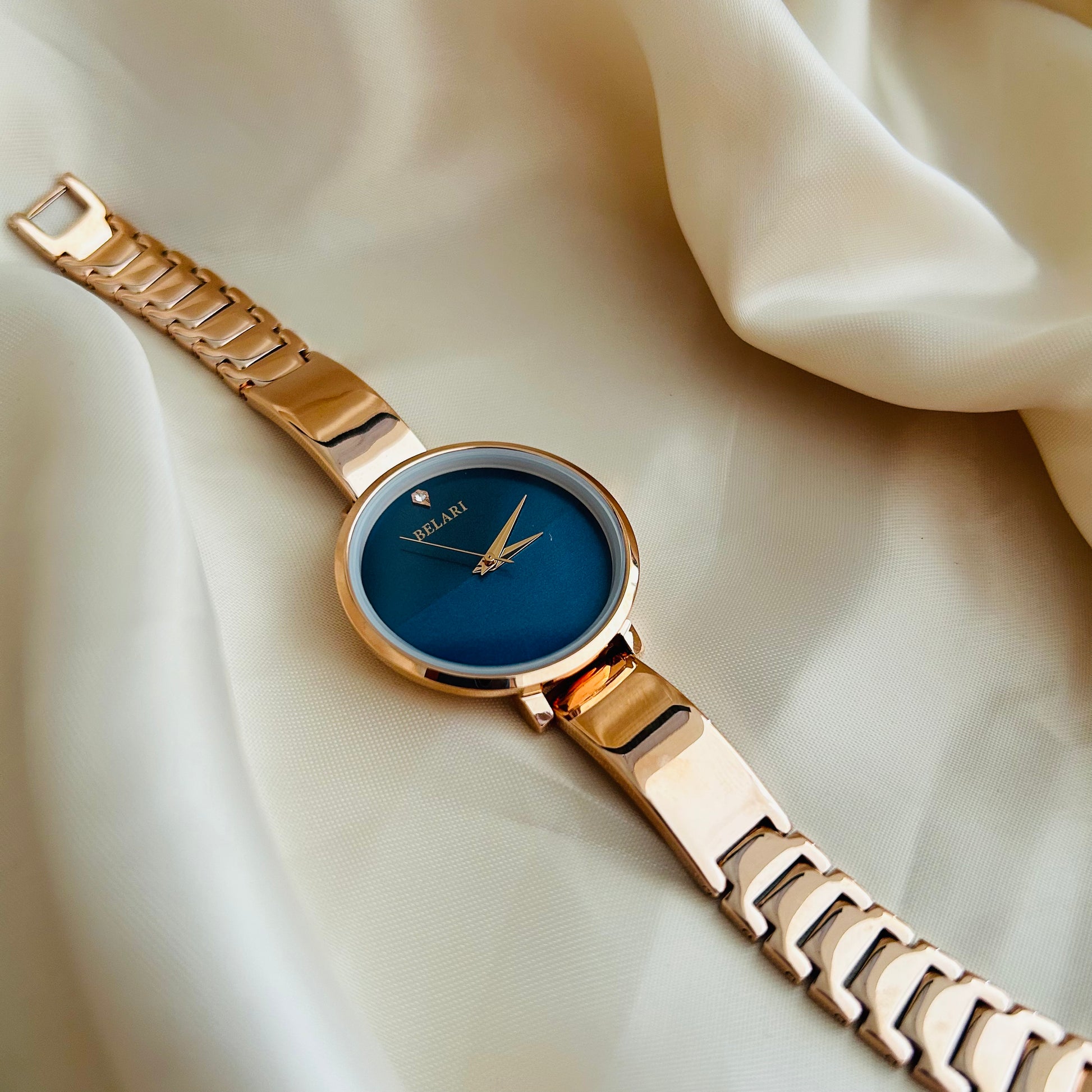 Rose gold wristwatch with round dial placed on satin fabric background.