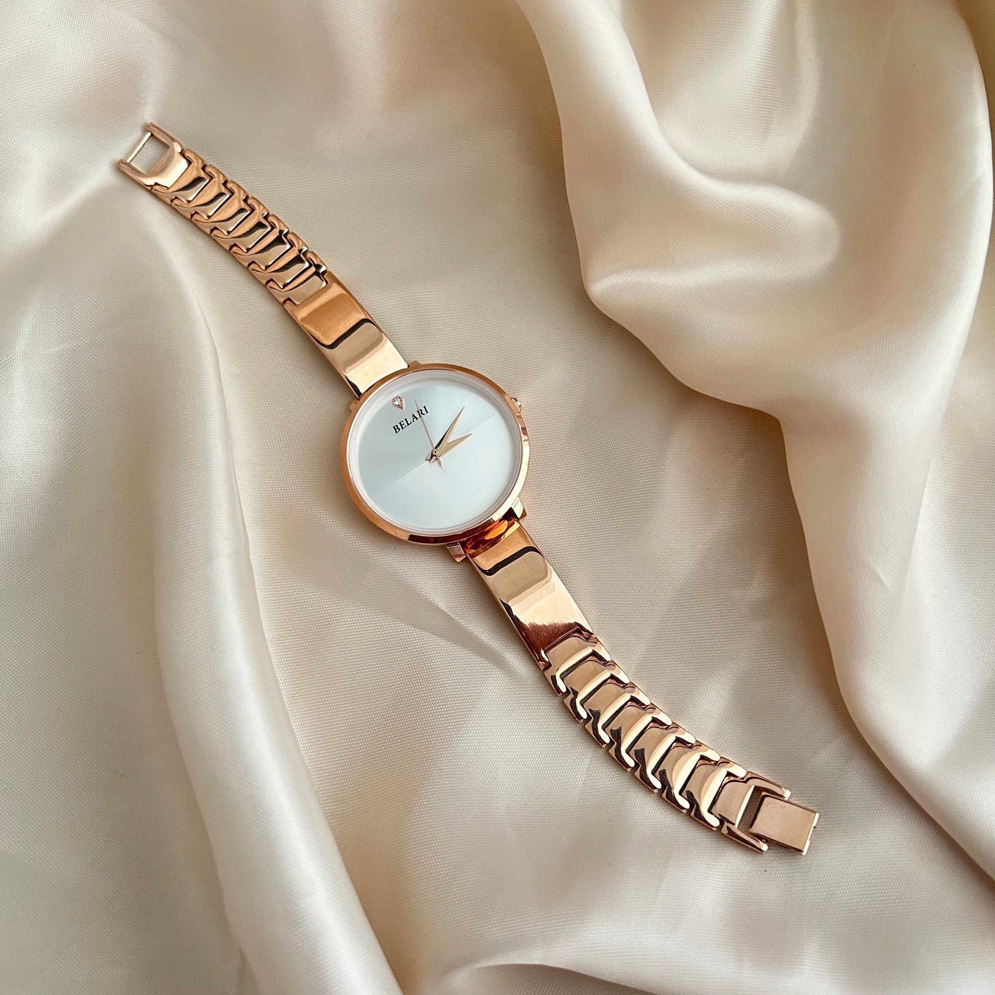 Rose gold wristwatch with round dial placed on satin fabric background.