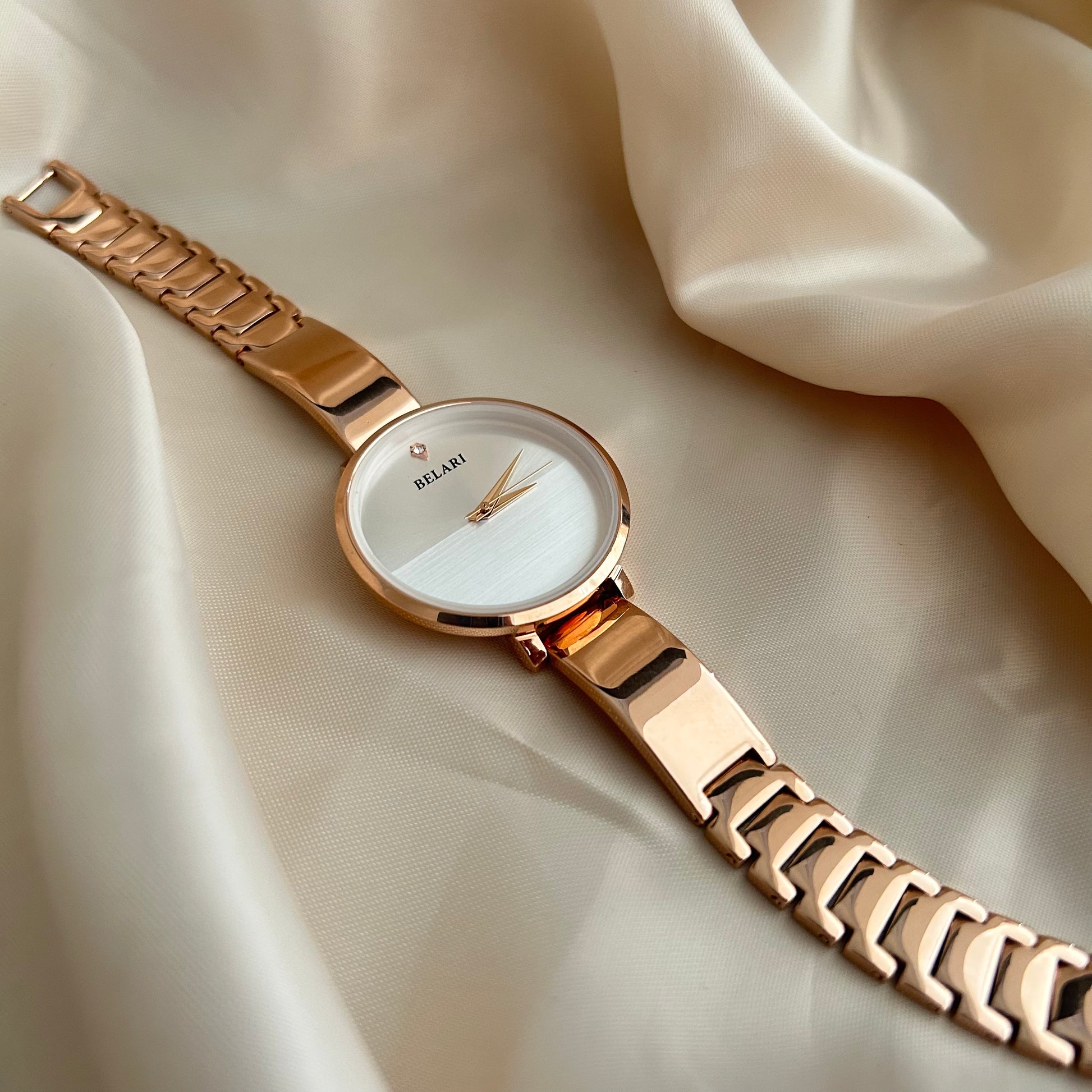 Rose gold wristwatch with round dial placed on satin fabric background.