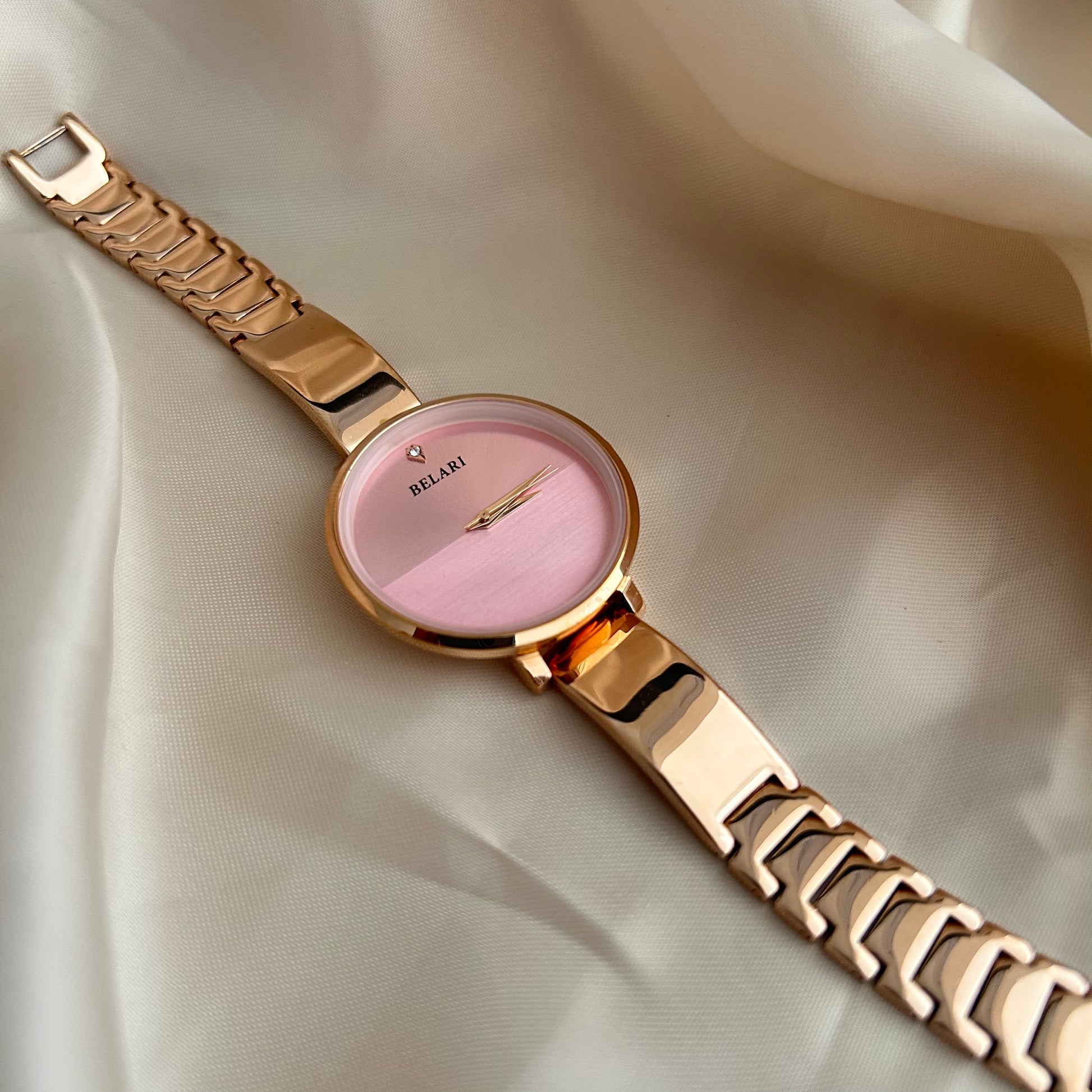 Rose gold wristwatch with round dial placed on satin fabric background.