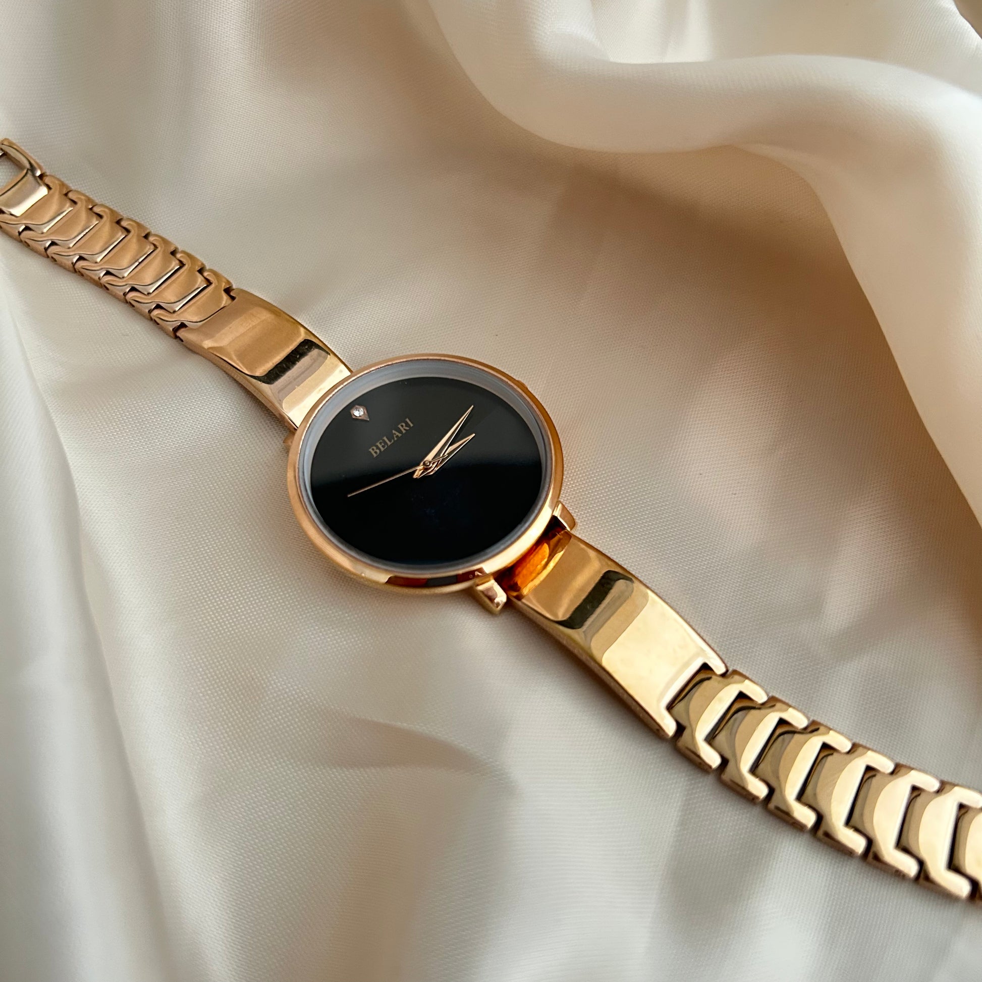 Rose gold wristwatch with round dial placed on satin fabric background.