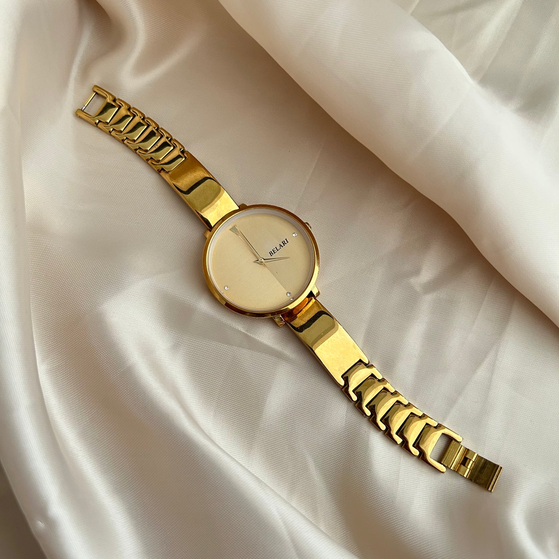 Gold wristwatch with simple dial and metal strap on neutral satin background.