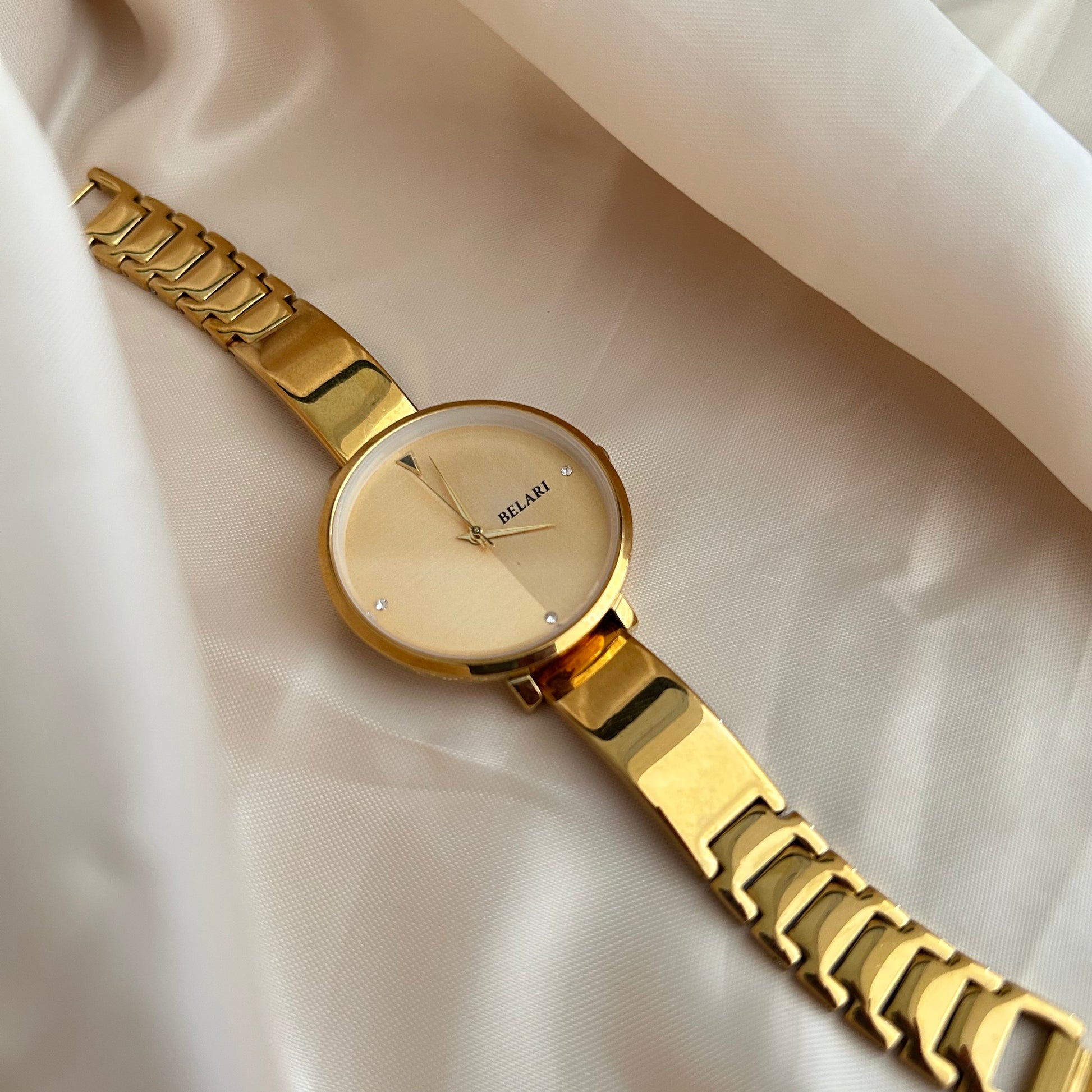 Gold wristwatch with simple dial and metal strap on neutral satin background.