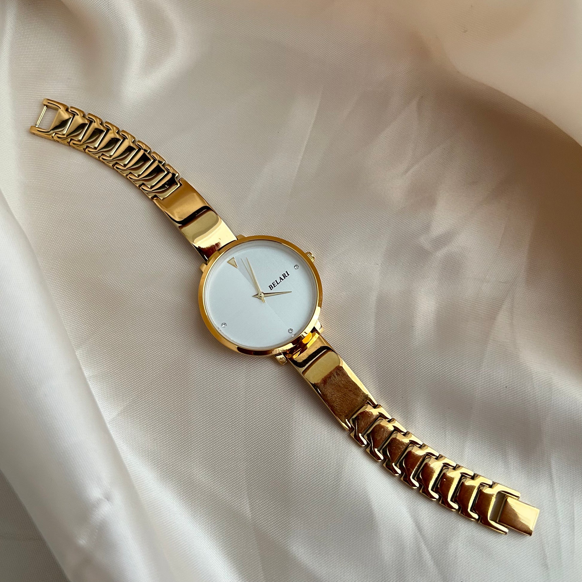Gold wristwatch with simple dial and metal strap on neutral satin background.