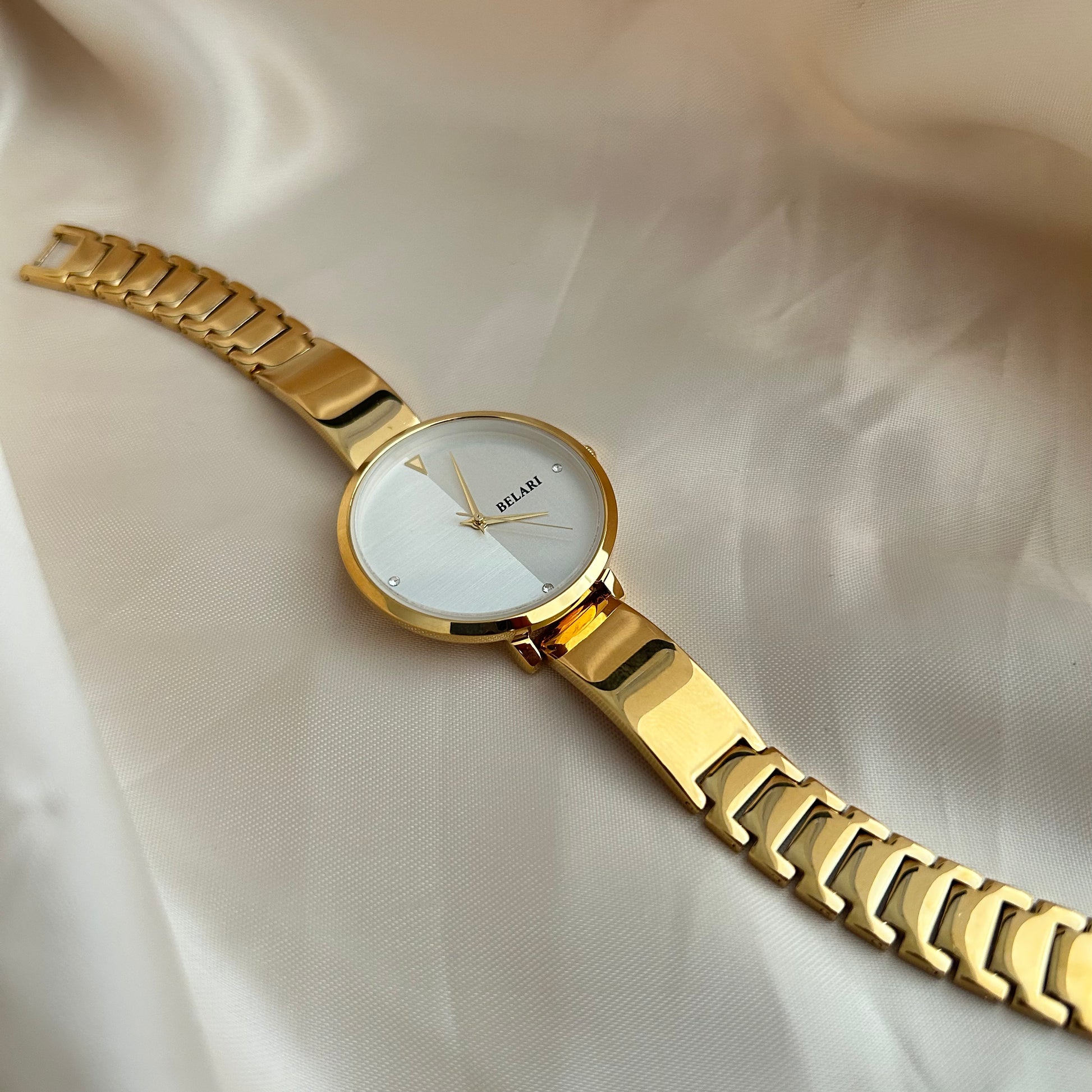 Gold wristwatch with simple dial and metal strap on neutral satin background.