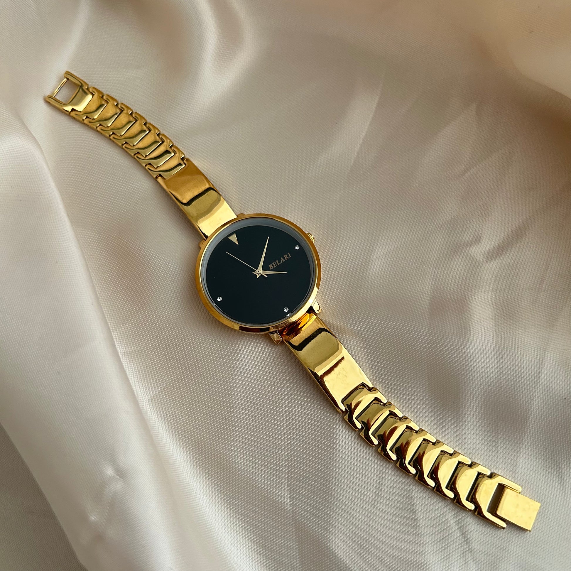 Gold wristwatch with simple dial and metal strap on neutral satin background.