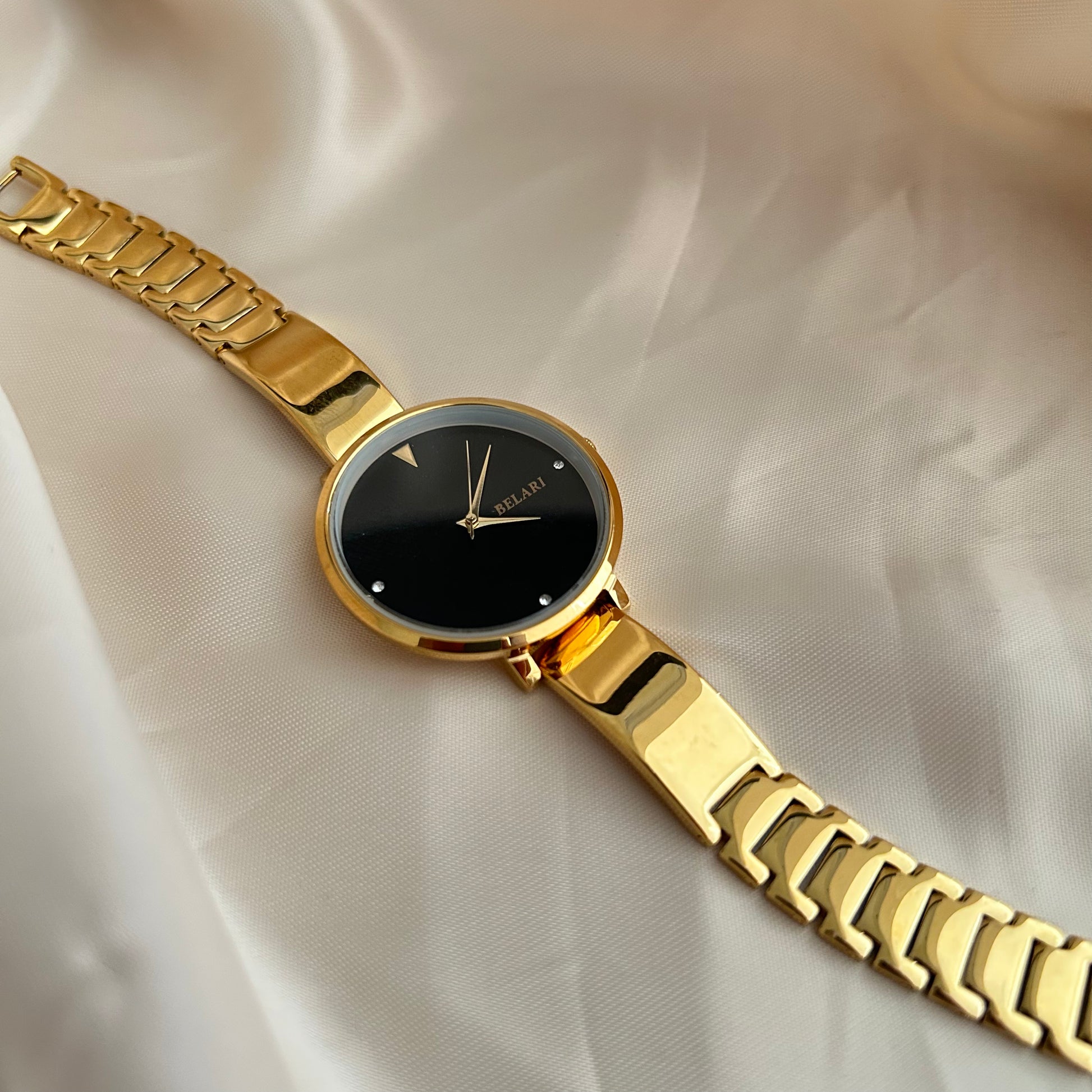 Gold wristwatch with simple dial and metal strap on neutral satin background.