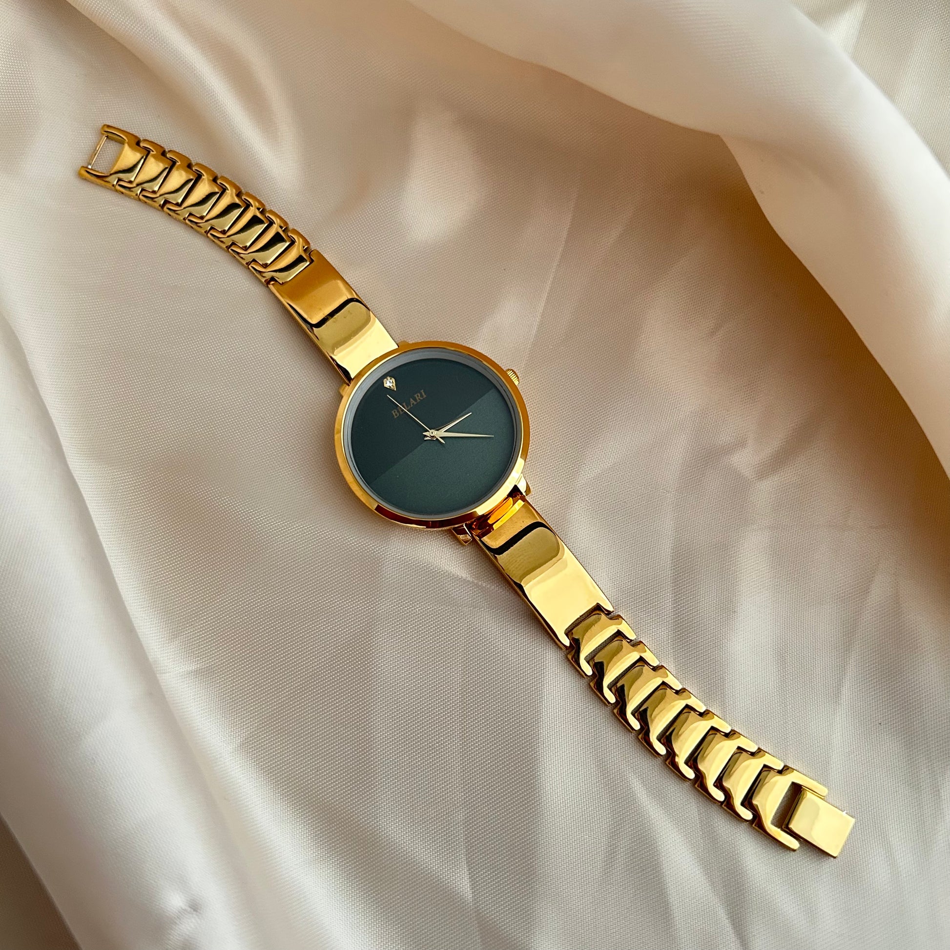 Gold wristwatch with simple dial and metal strap on neutral satin background.