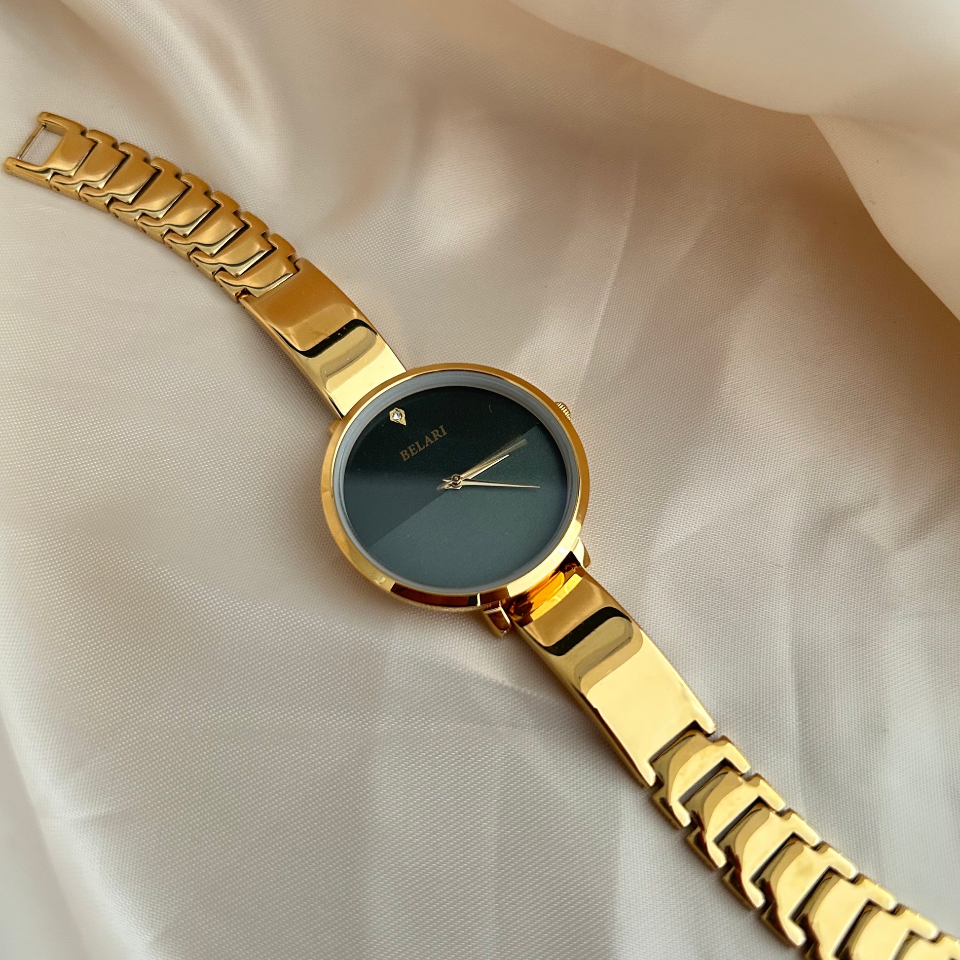 Gold wristwatch with simple dial and metal strap on neutral satin background.