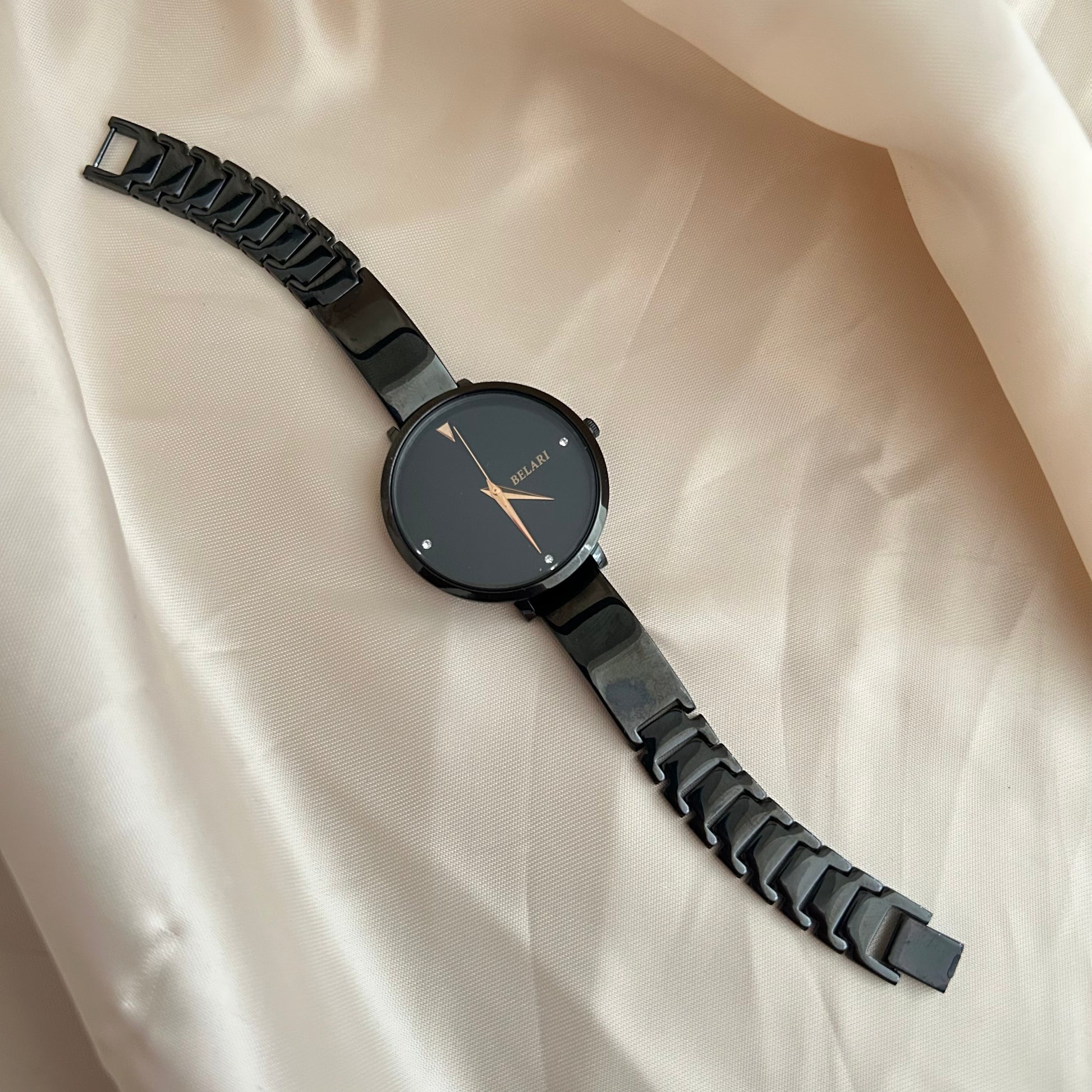 Black dial wristwatch with dark strap placed on satin cloth background.