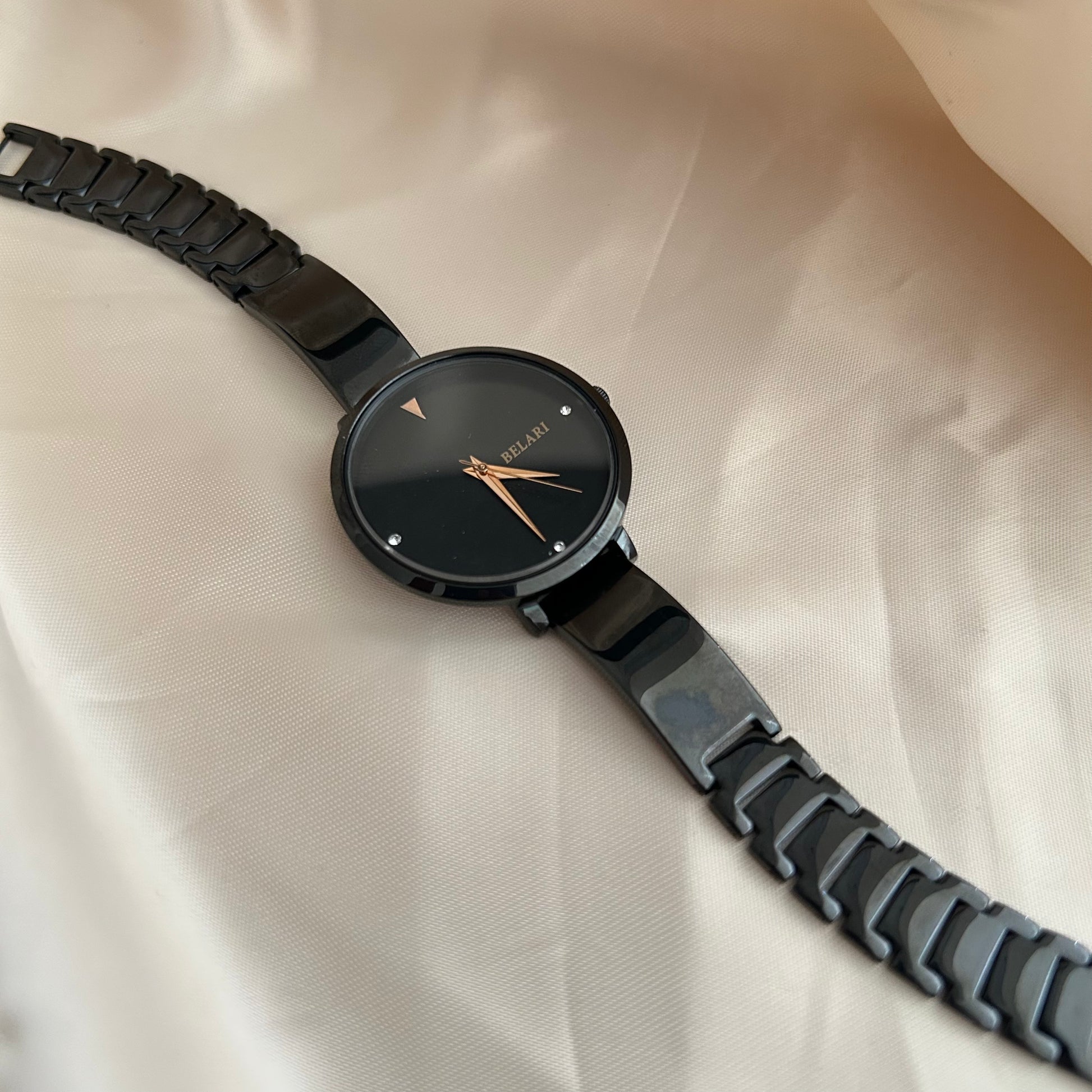 Black dial wristwatch with dark strap placed on satin cloth background.