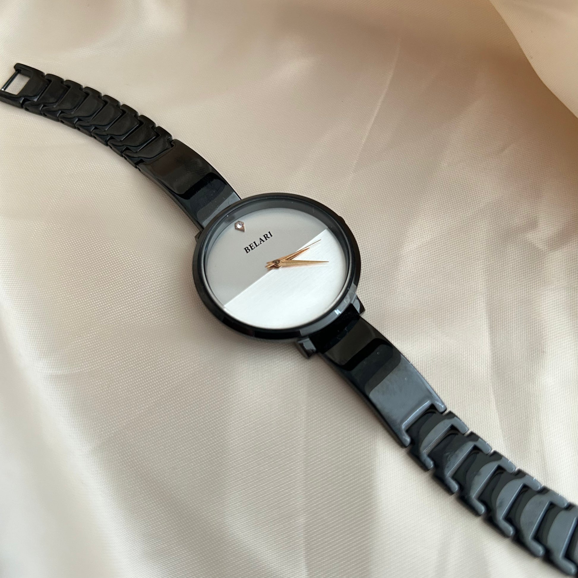 Black dial wristwatch with dark strap placed on satin cloth background.