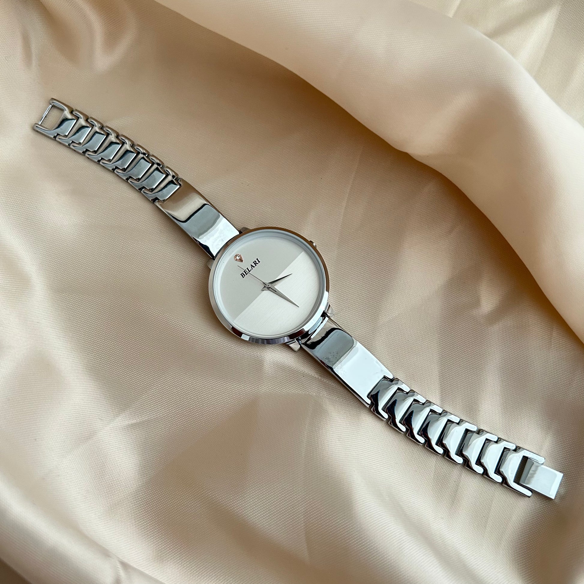 Silver Body wristwatch with silver strap on soft fabric background.