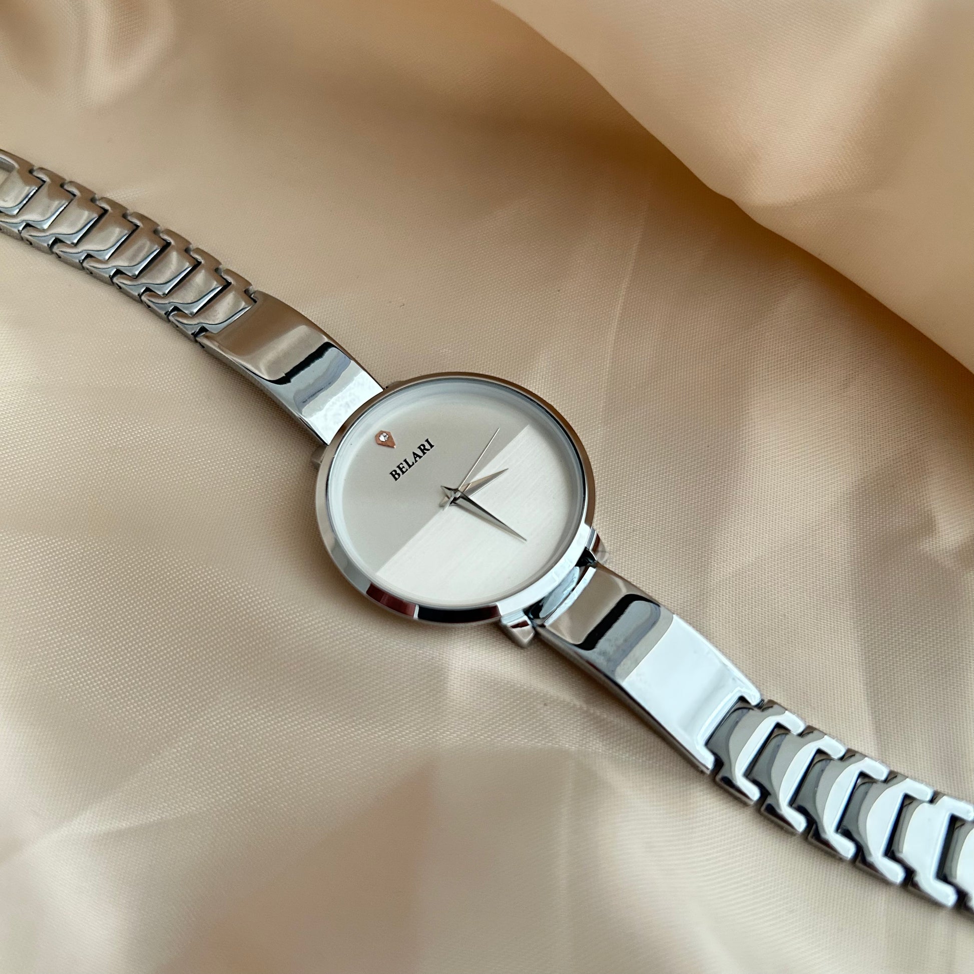 Silver Body wristwatch with silver strap on soft fabric background.