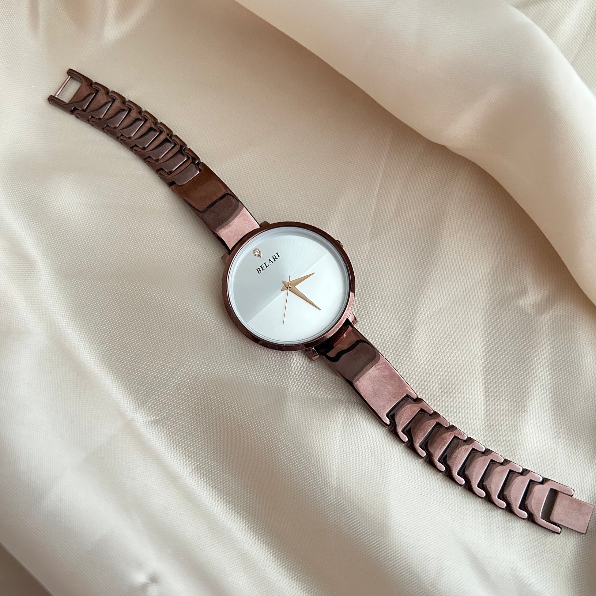 Rose tone wristwatch with minimal dial placed on satin cloth background.