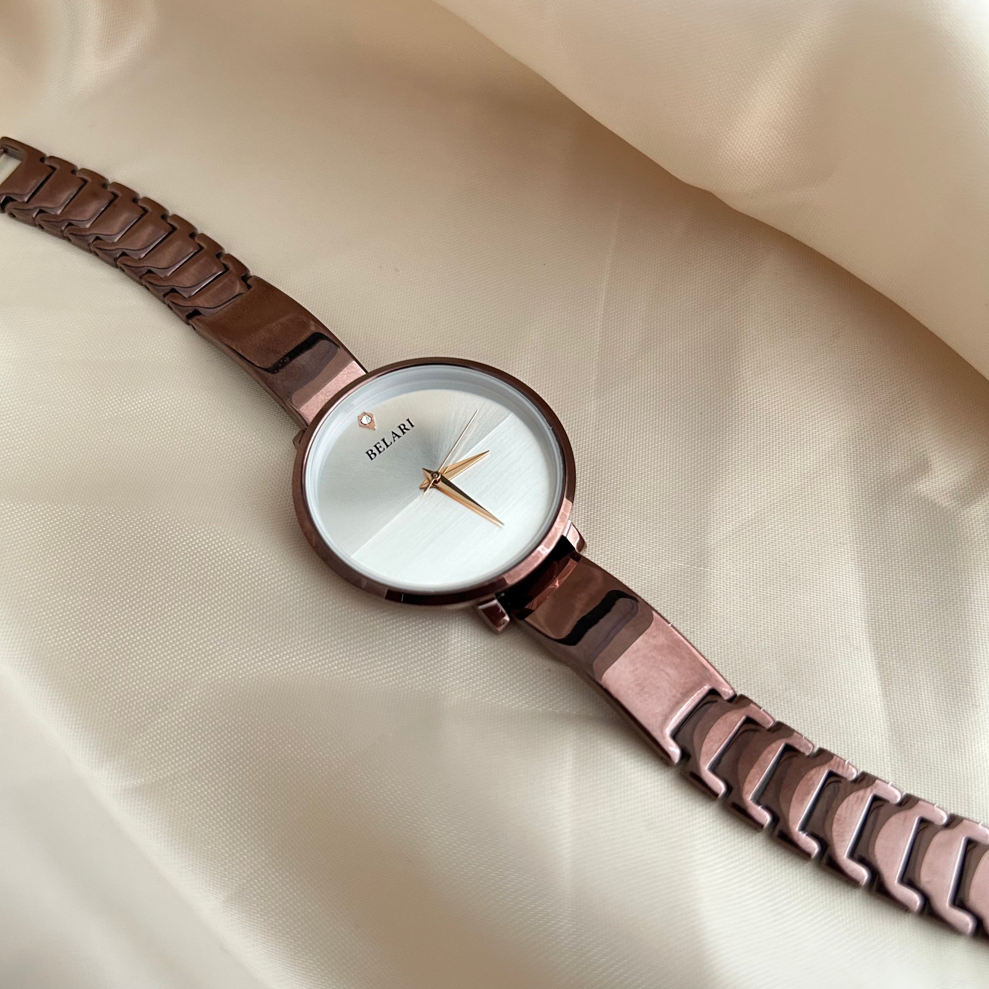 Rose tone wristwatch with minimal dial placed on satin cloth background.