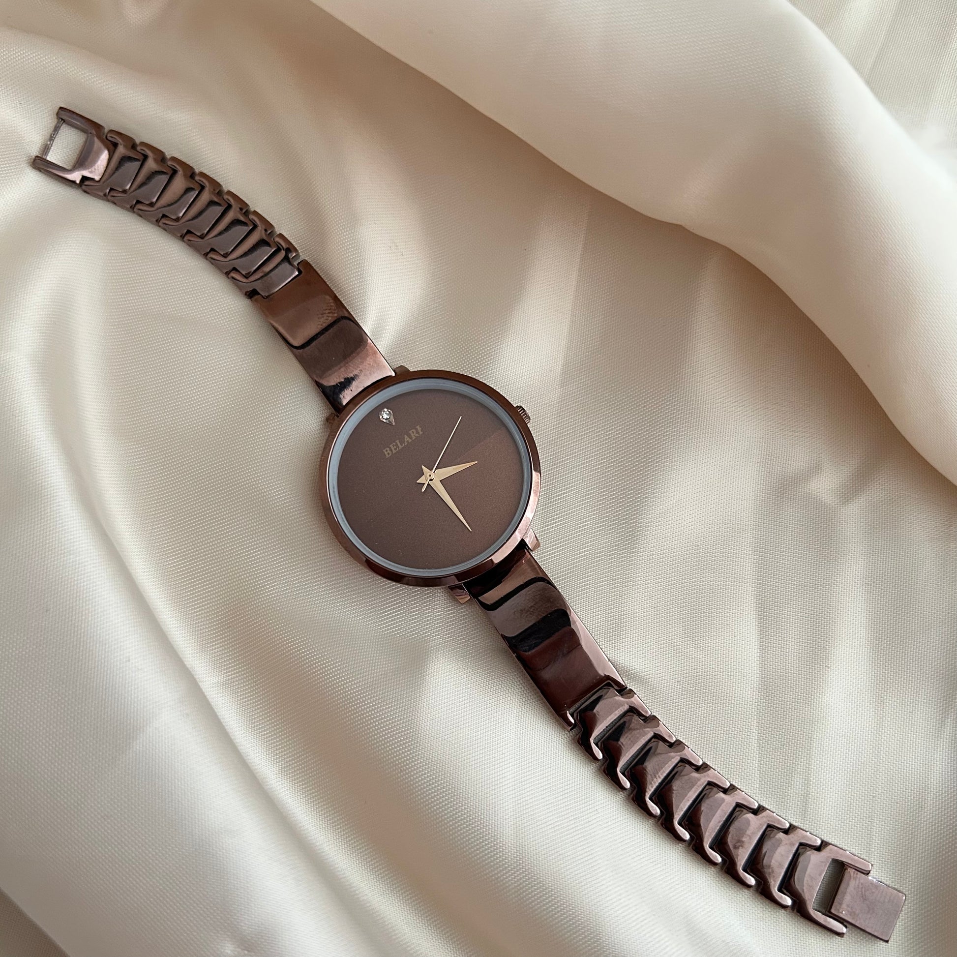 Rose tone wristwatch with minimal dial placed on satin cloth background.