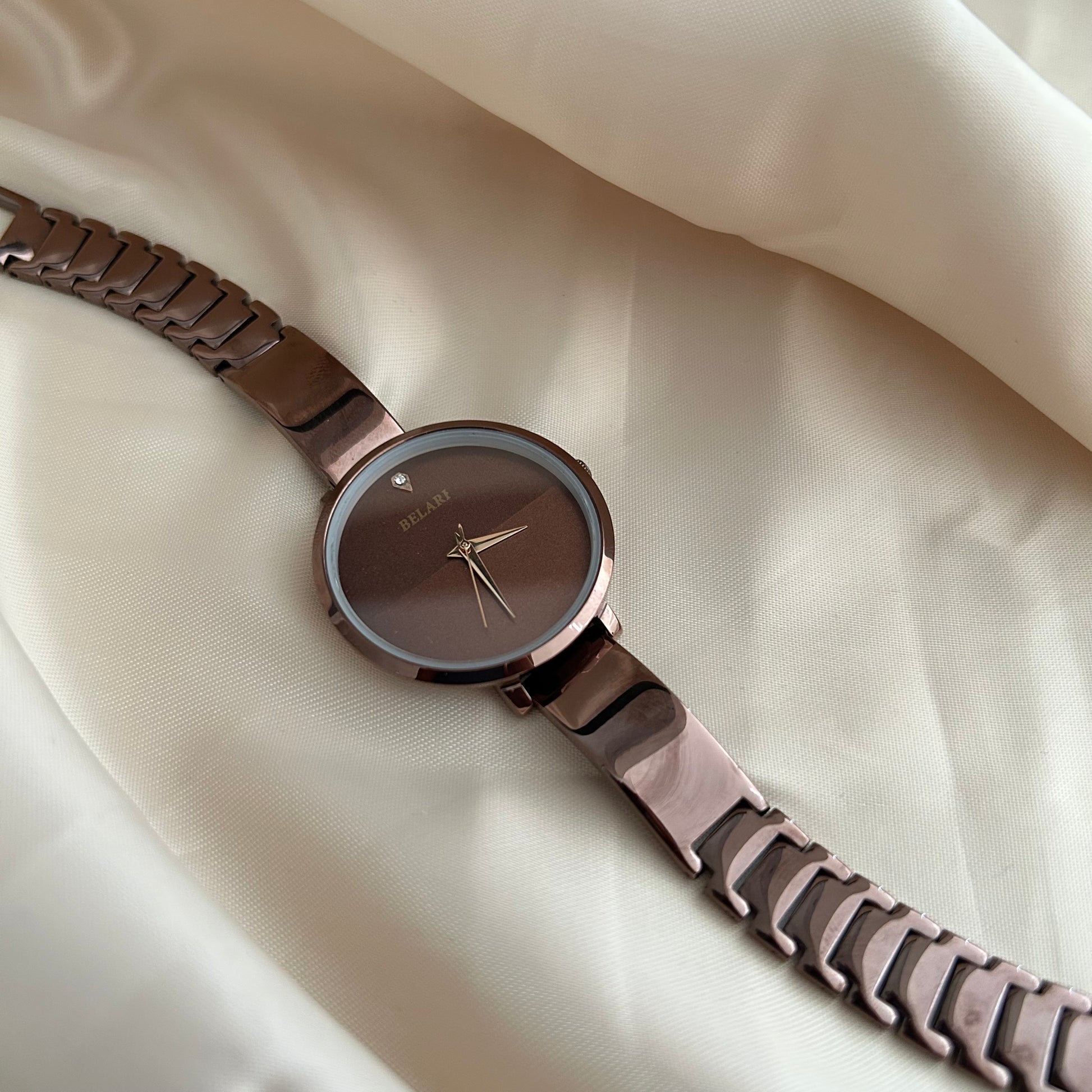Rose tone wristwatch with minimal dial placed on satin cloth background.