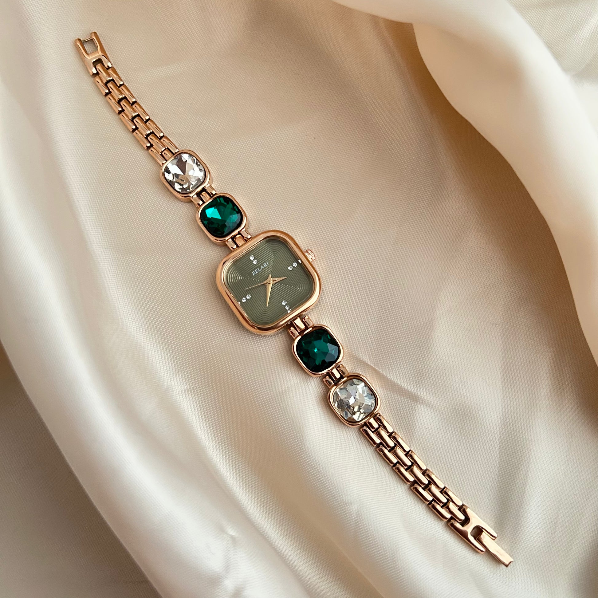 Gold wristwatch with gemstone bracelet links and square dial on satin background.