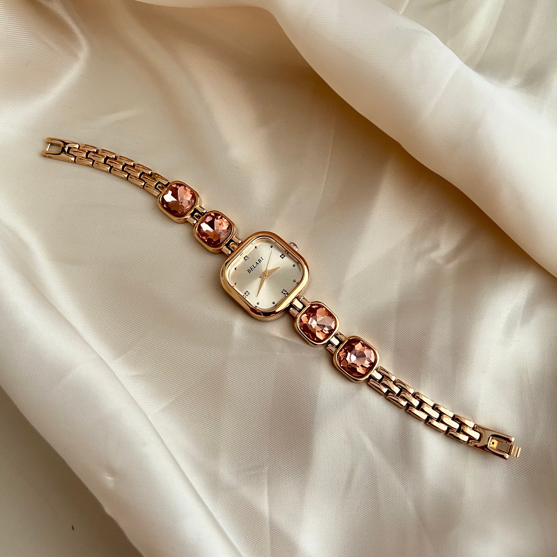 Gold wristwatch with gemstone bracelet links and square dial on satin background.