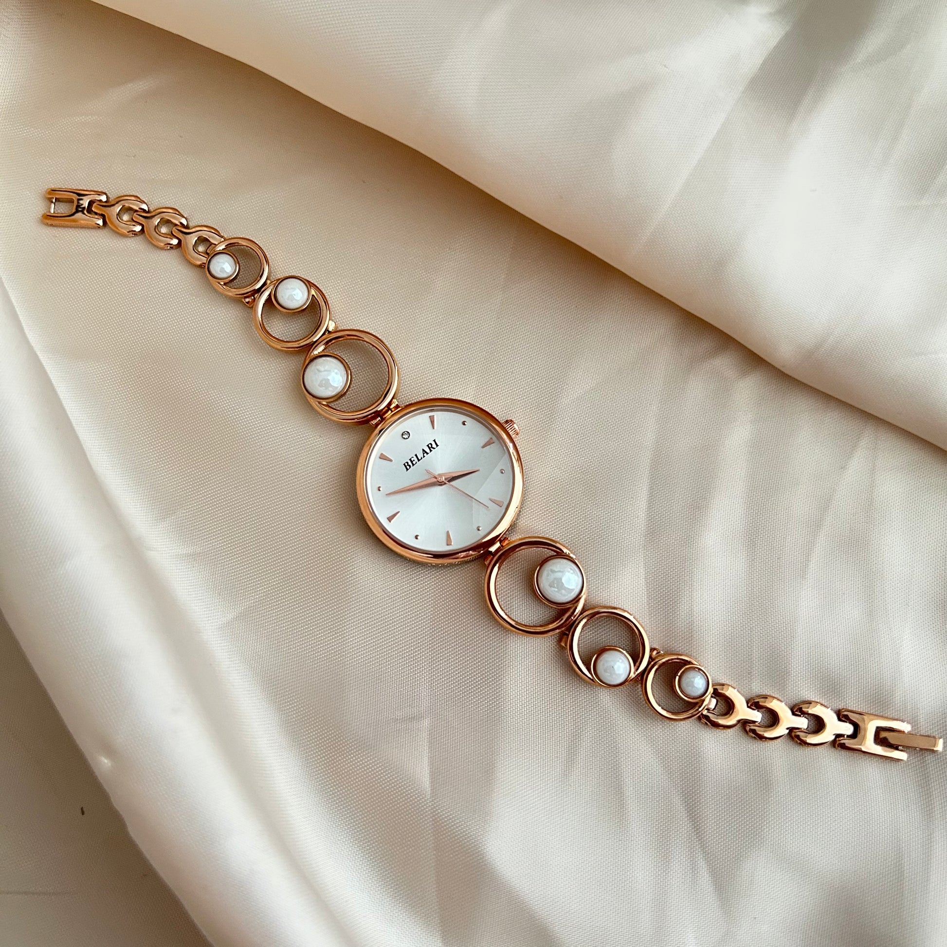 Rose gold wristwatch with pearl bracelet design and round dial on soft satin background.