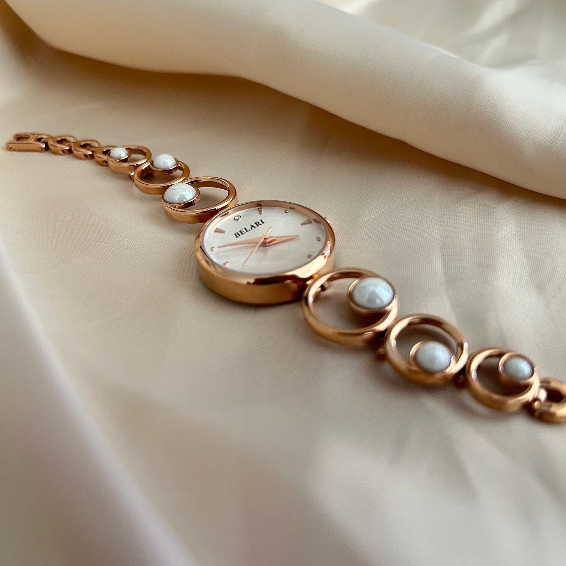 Rose gold wristwatch with pearl bracelet design and round dial on soft satin background.