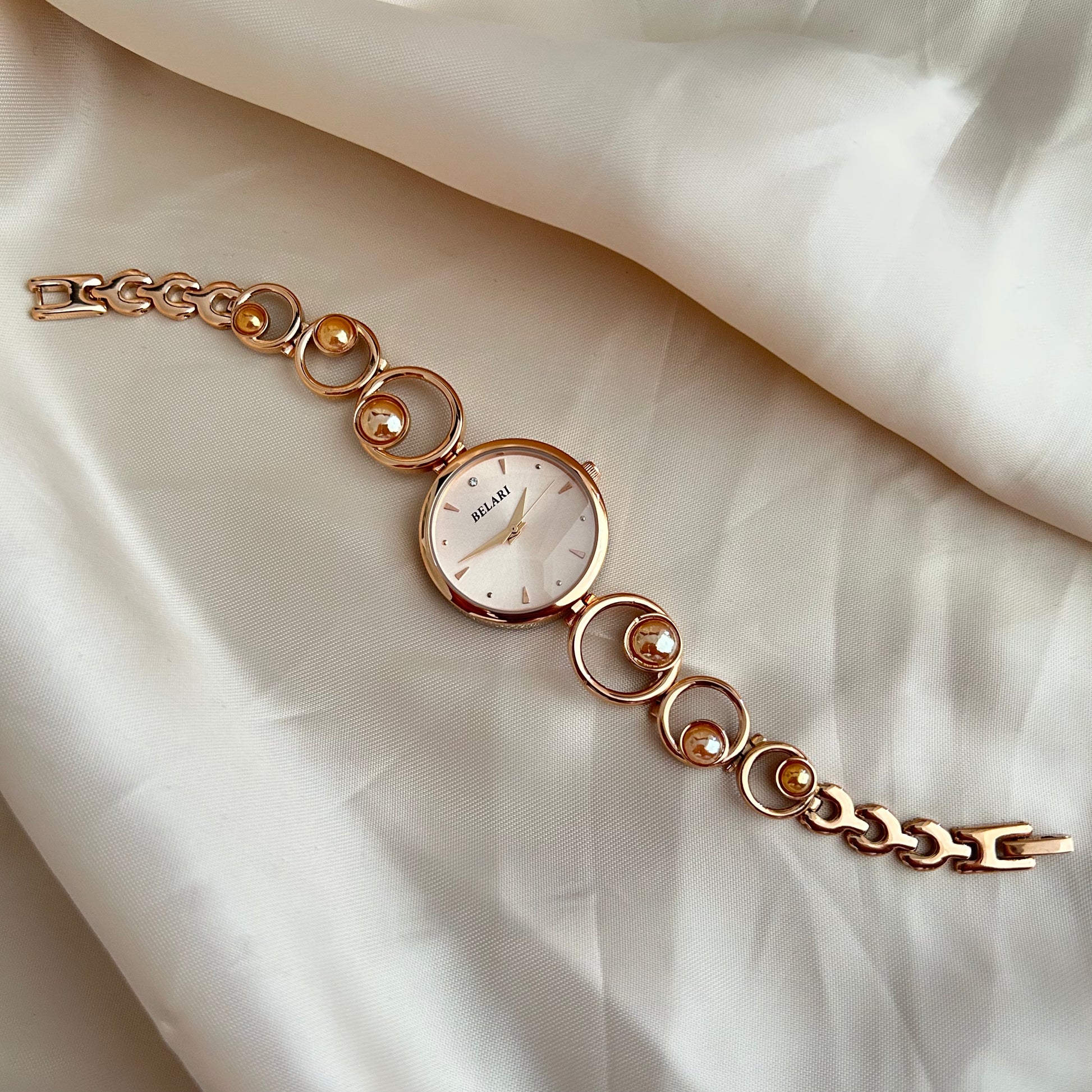 Rose gold wristwatch with pearl bracelet design and round dial on soft satin background.