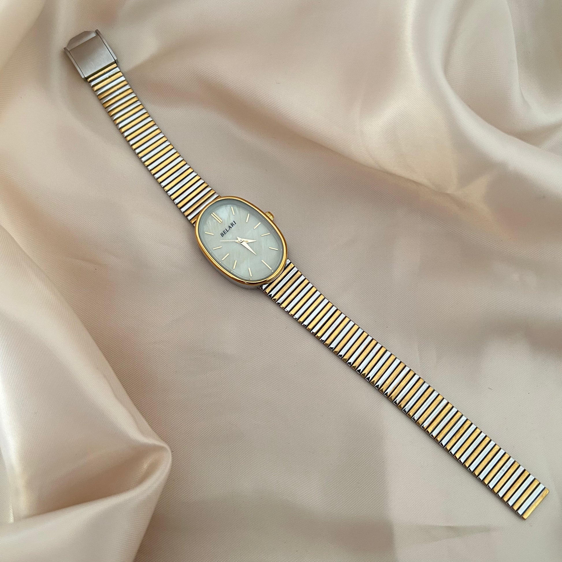 Gold and silver strap wristwatch with minimal dial placed on satin fabric.