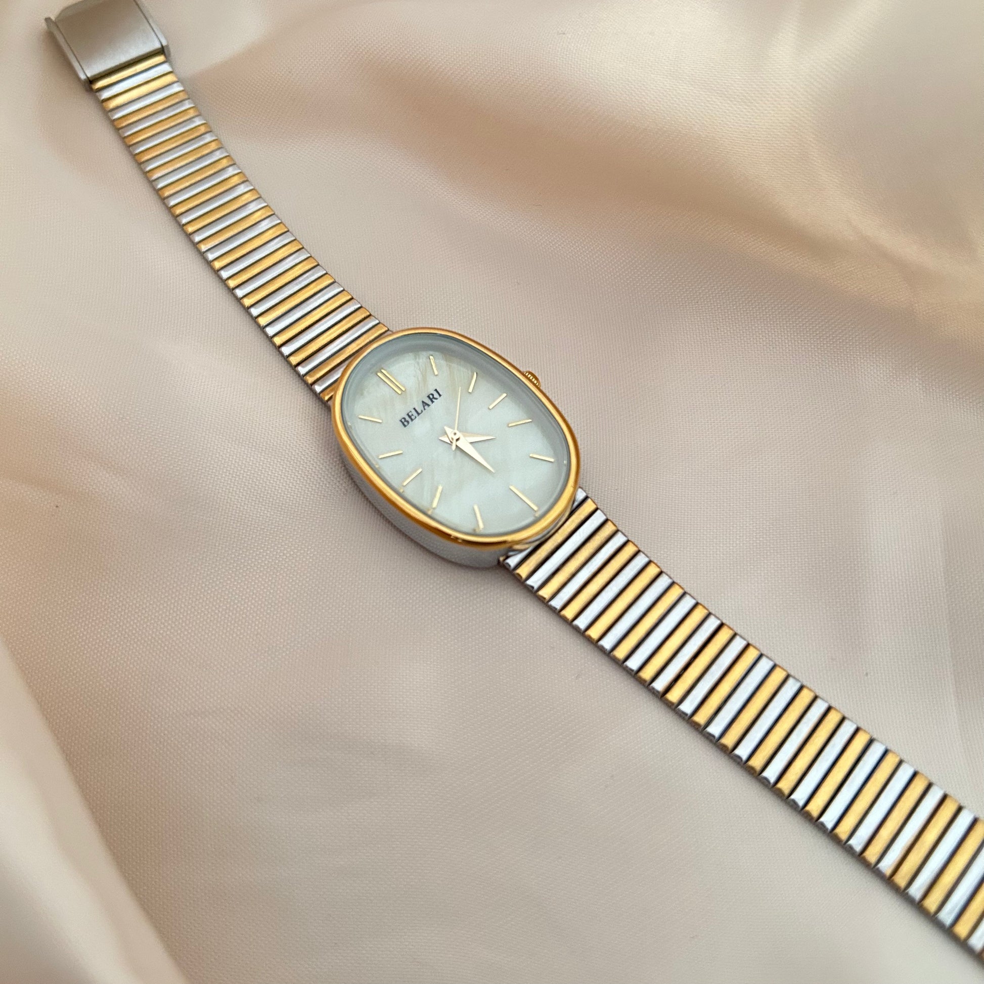 Gold and silver strap wristwatch with minimal dial placed on satin fabric.