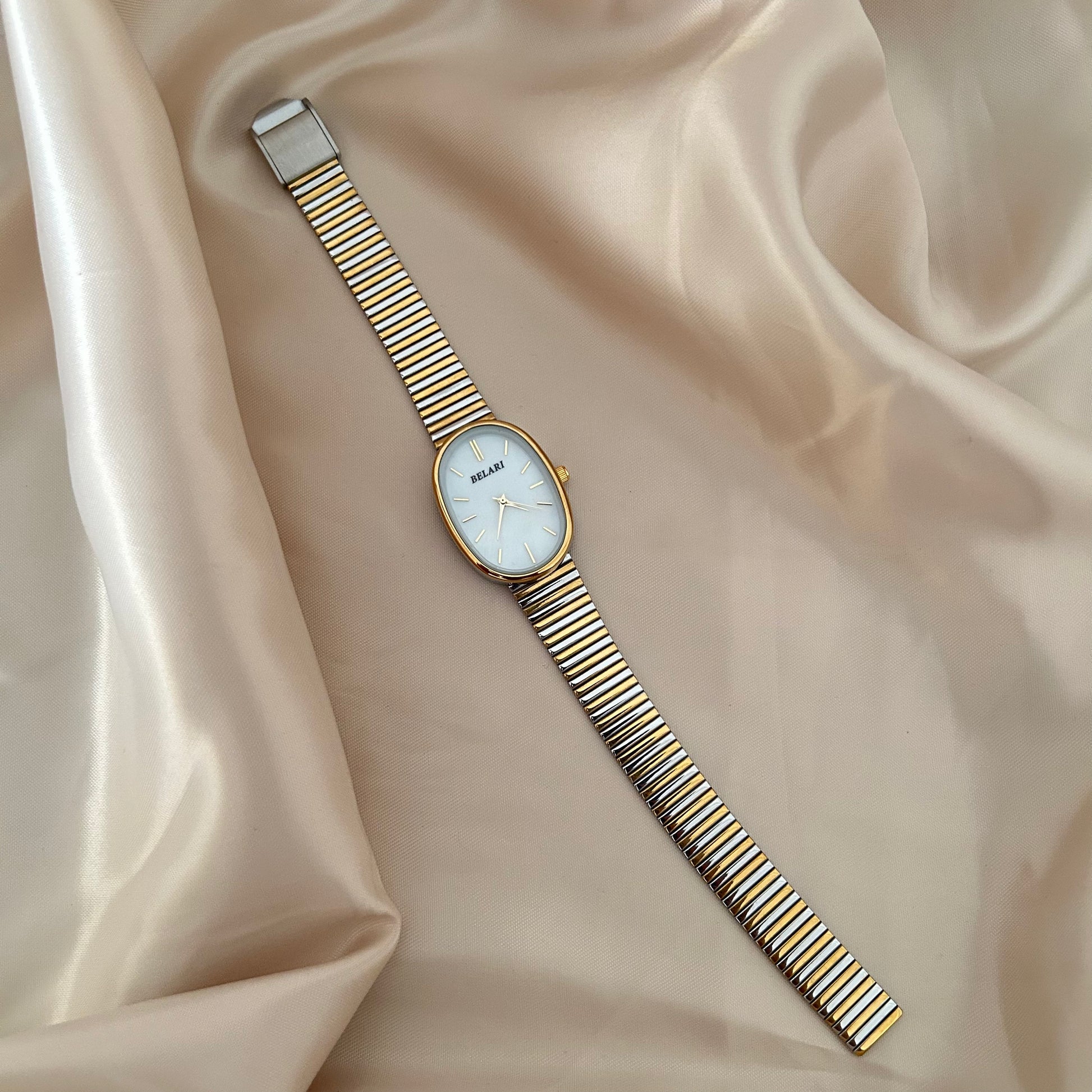 Gold and silver strap wristwatch with minimal dial placed on satin fabric.
