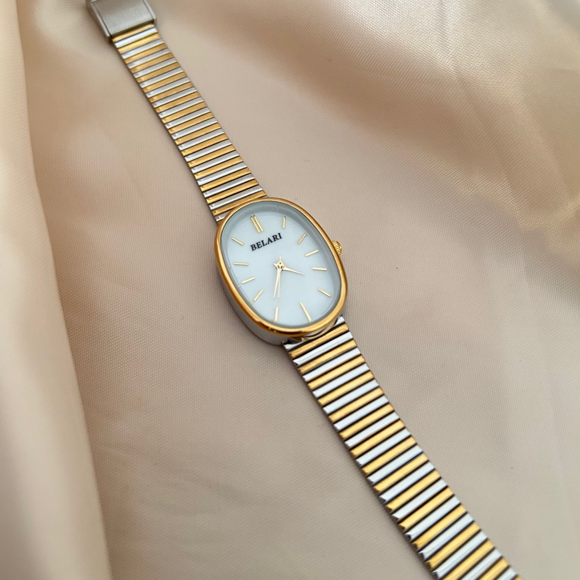 Gold and silver strap wristwatch with minimal dial placed on satin fabric.