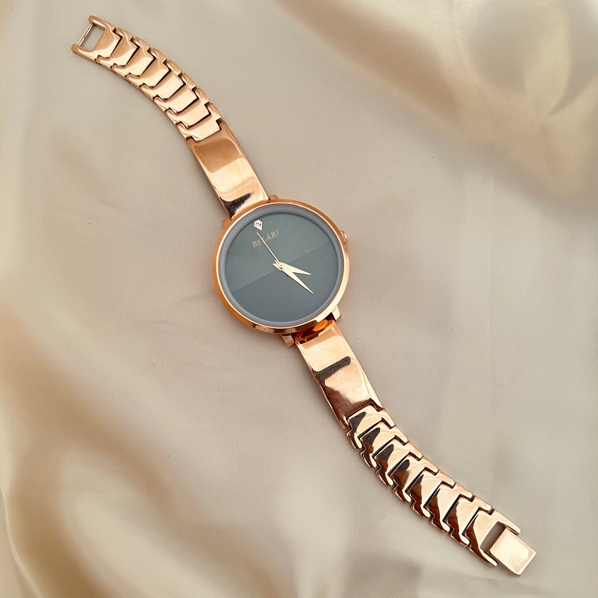 Rose gold wristwatch with round dial placed on satin fabric background.