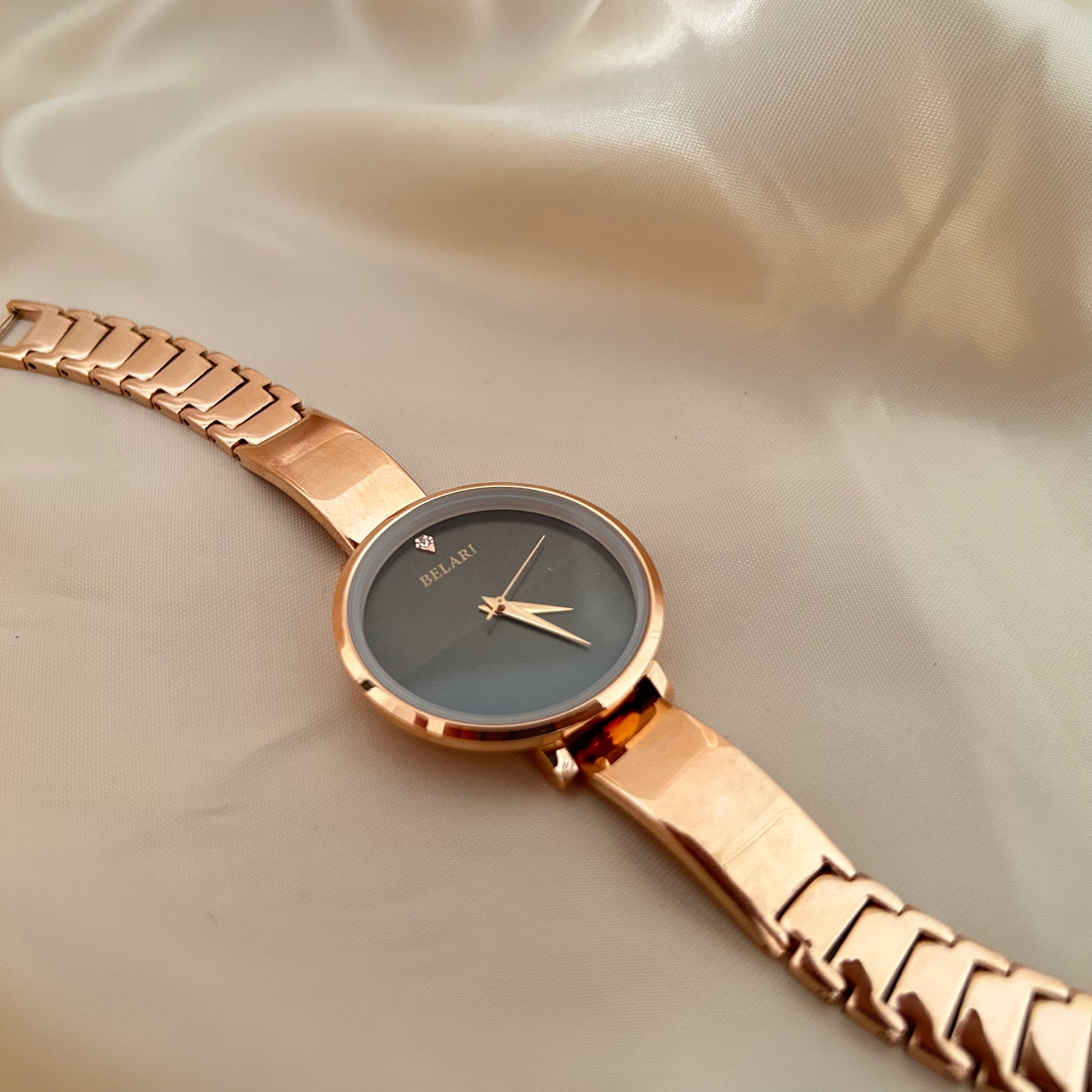 Rose gold wristwatch with round dial placed on satin fabric background.