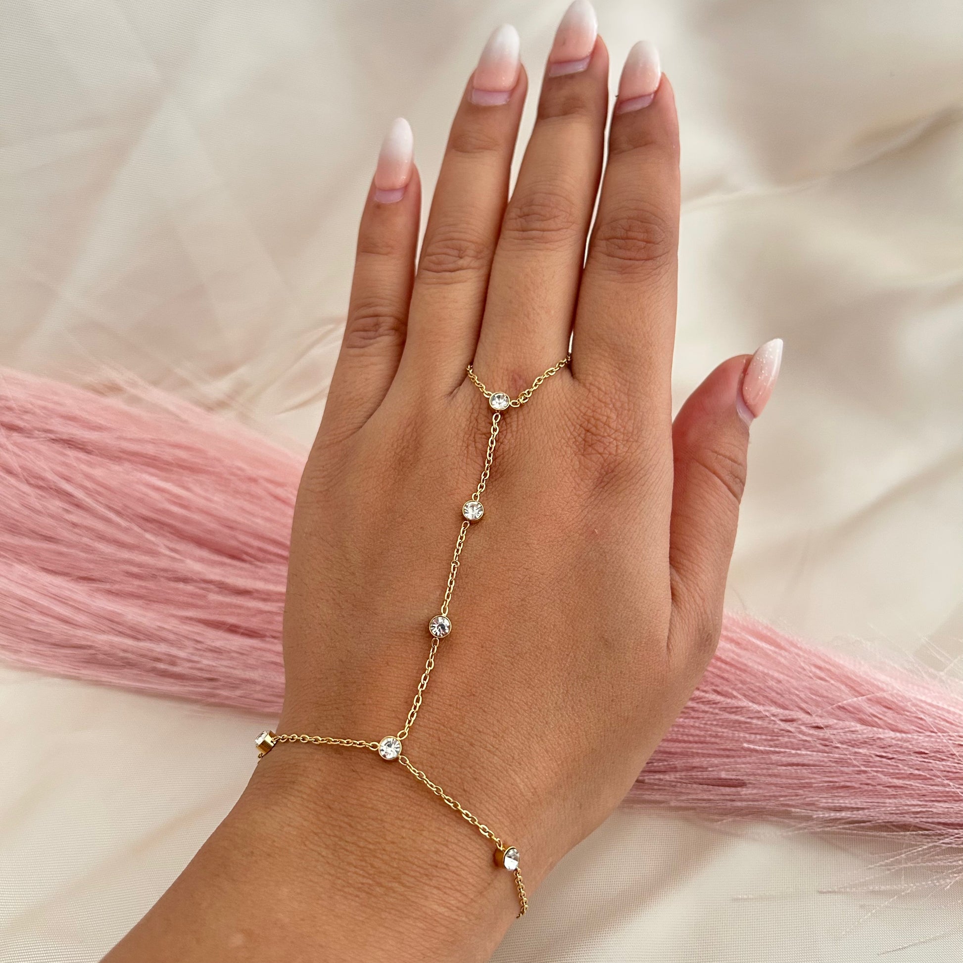 Minimal gold hand chain with small round stones connecting finger and wrist