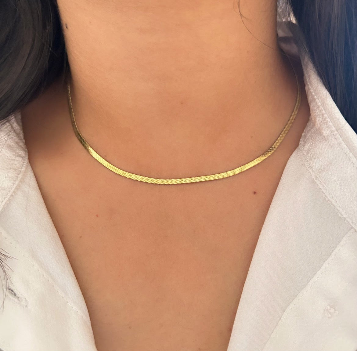 Flat gold herringbone chain necklace displayed on pink background