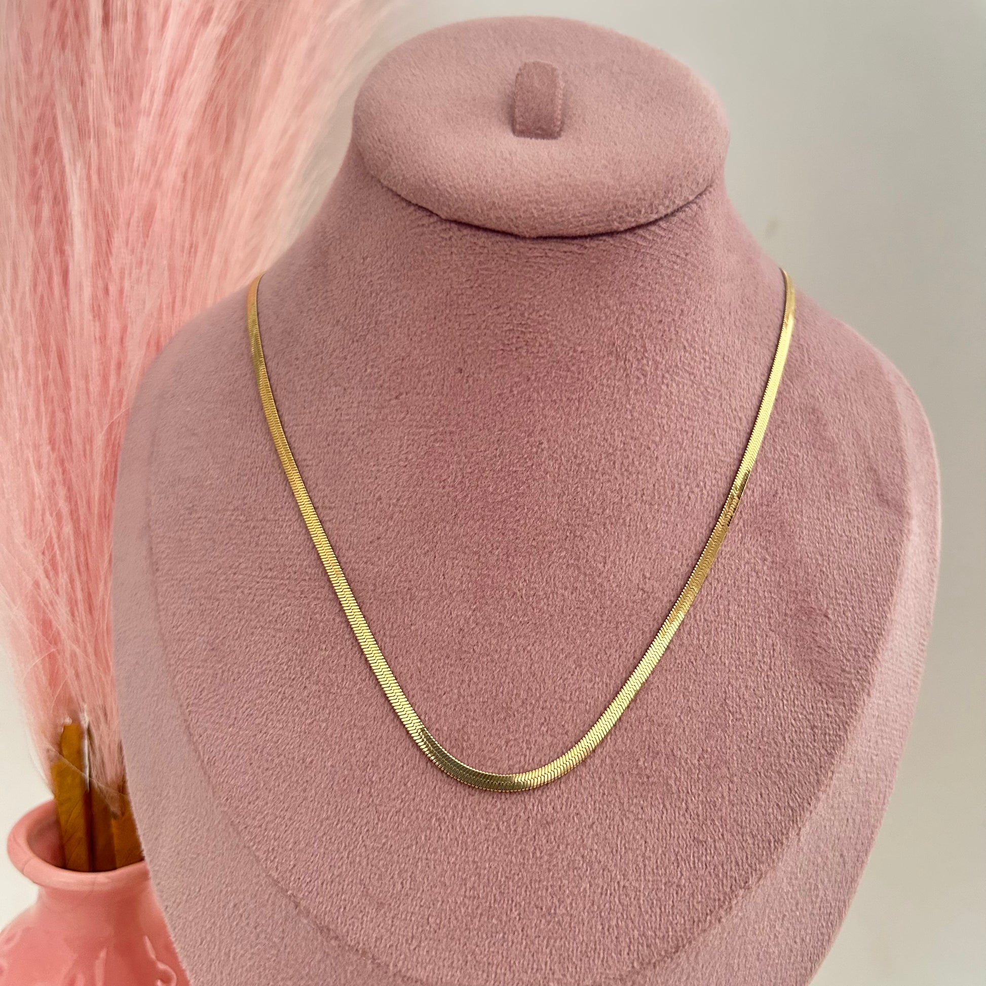 Flat gold herringbone chain necklace displayed on pink background