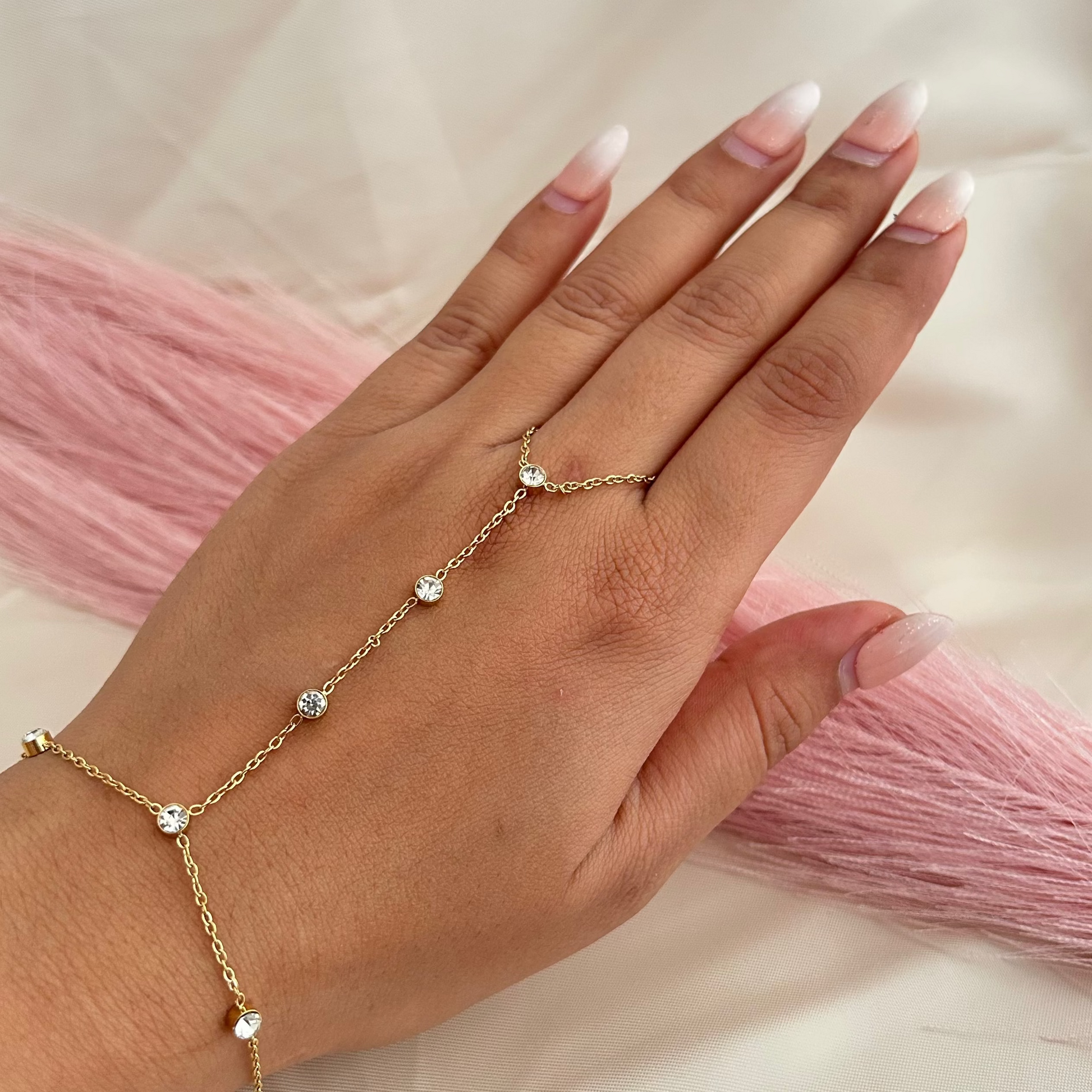 Minimal gold hand chain with small round stones connecting finger and wrist