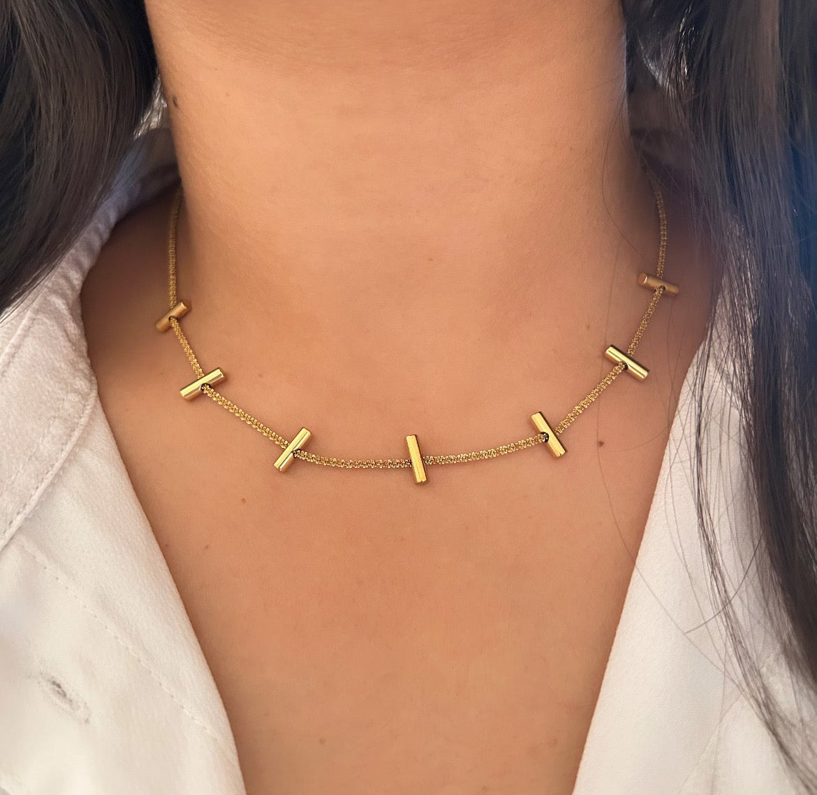 Gold necklace with small horizontal bar charms evenly spaced on chain.