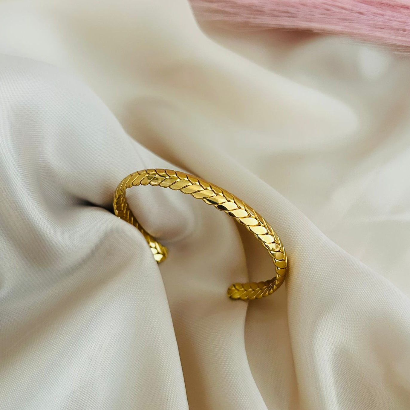 Gold open cuff bracelet with scale-textured pattern placed on soft satin fabric, minimal elegant jewelry design